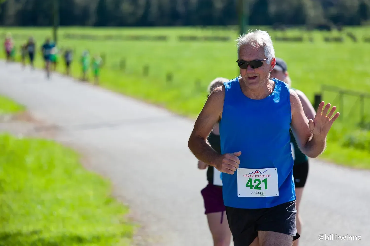 A man wearing a blue tank top with the number 421 on it is running a race.