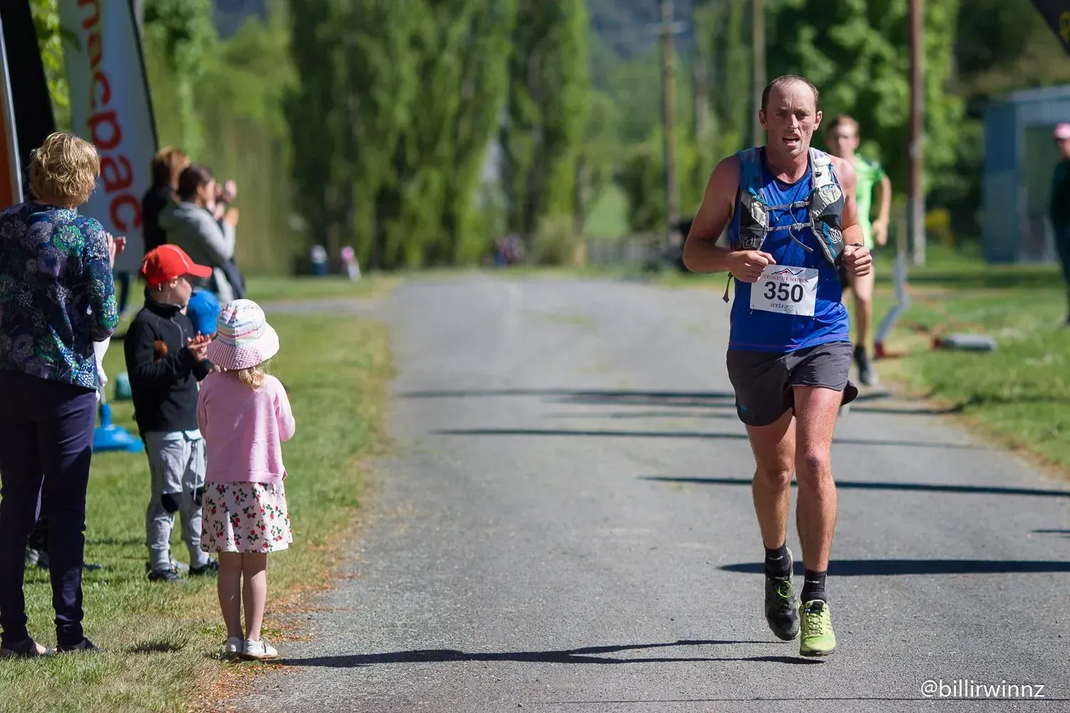 A man is running down a road while people watch.