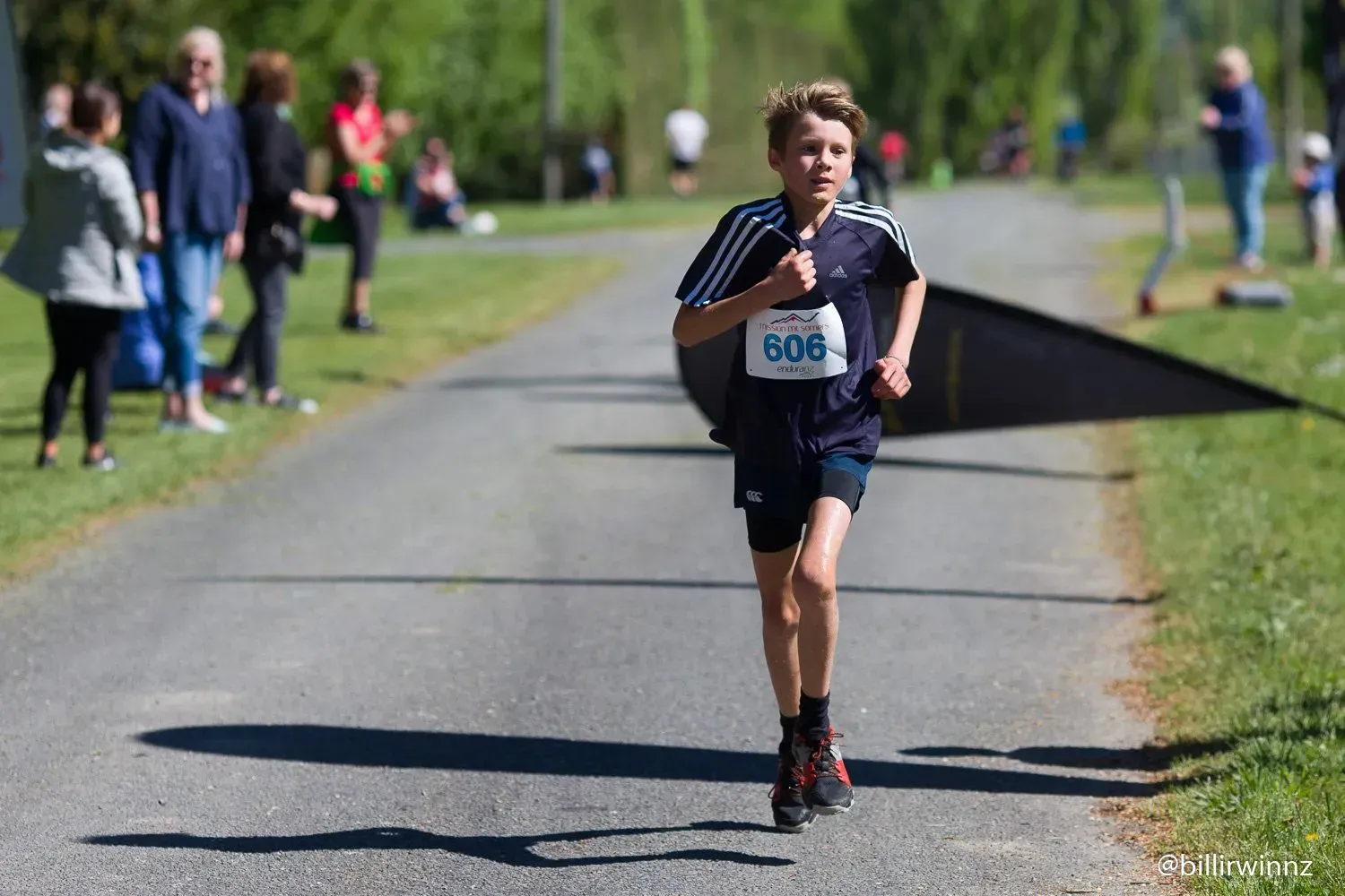 A young boy is running down a road with a number on his shirt.