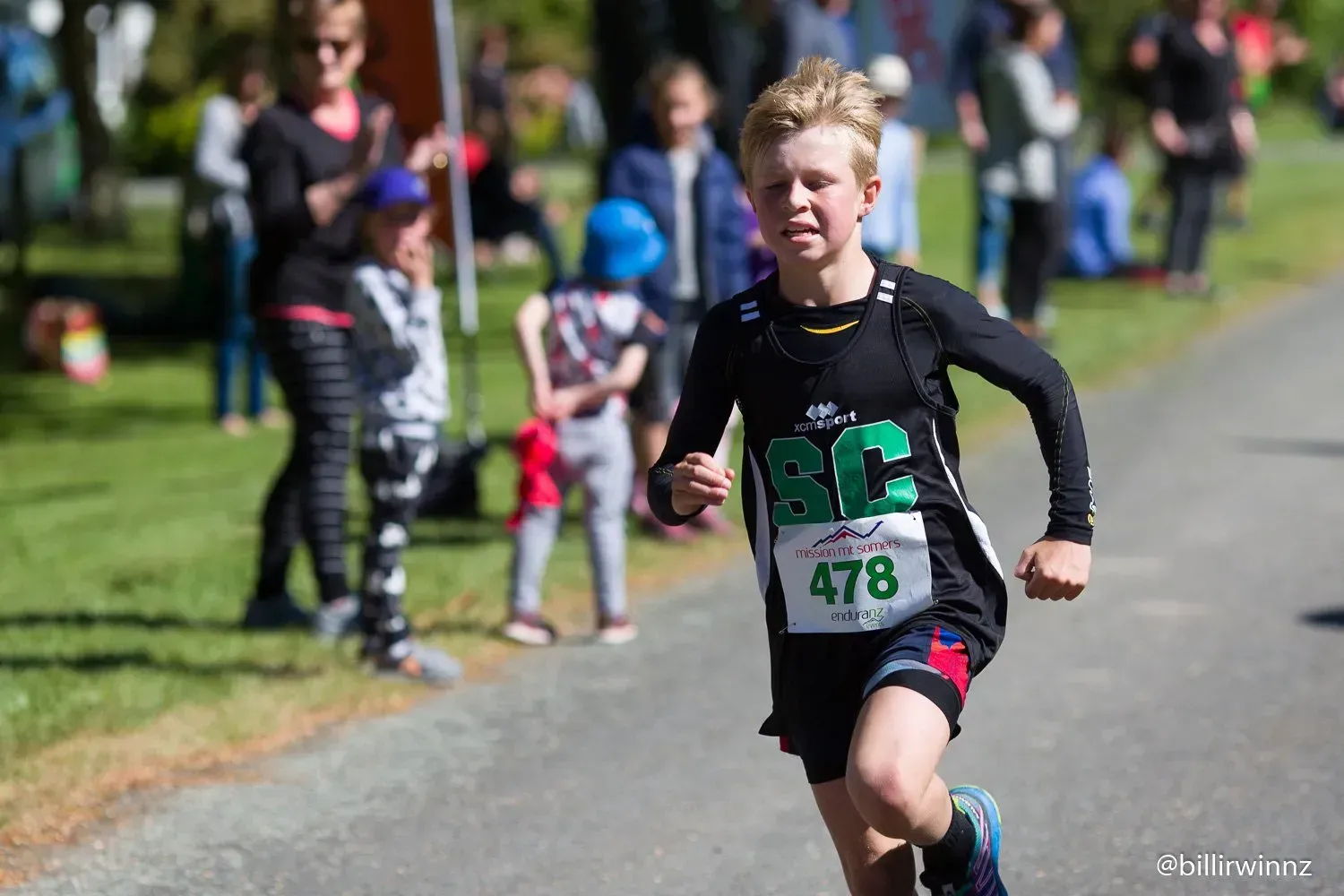 A young boy is running a marathon on a road.