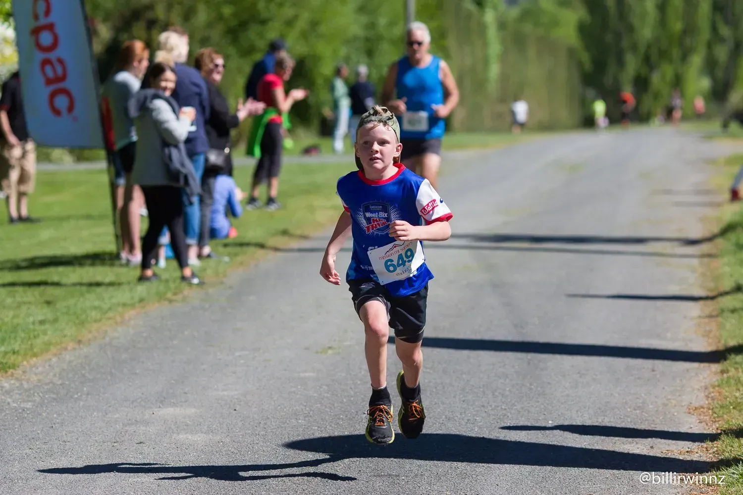 A young boy is running down a road in a race.