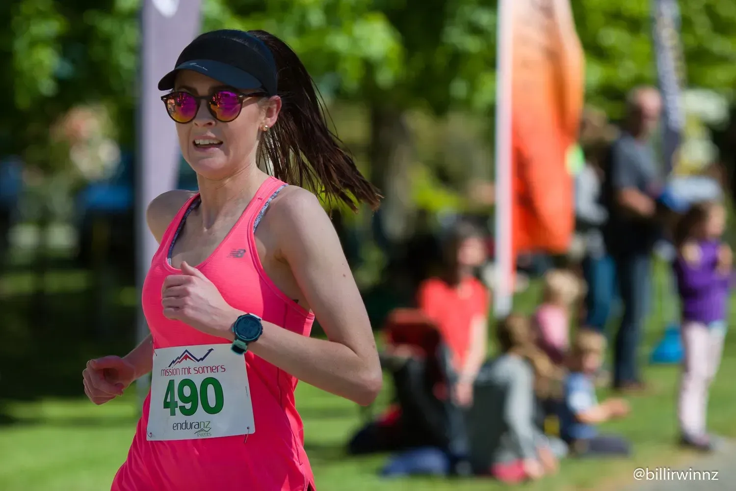 A woman in a pink tank top and sunglasses is running in a race.