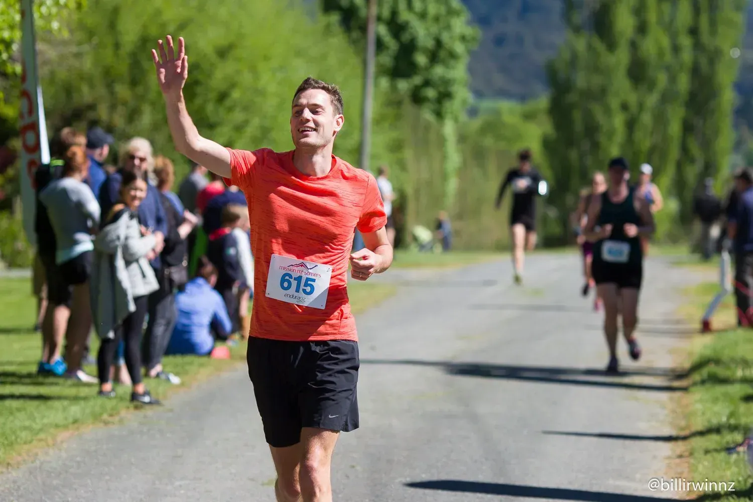 A man is running a marathon and waving at the crowd.