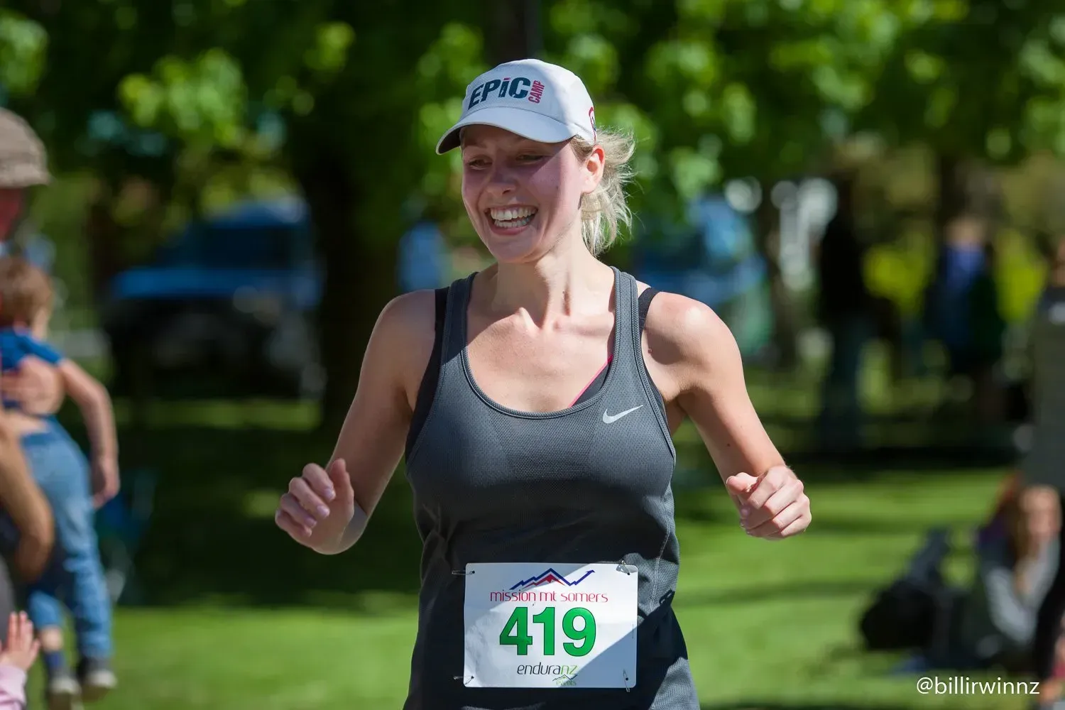 A woman is running a marathon in a park and smiling.