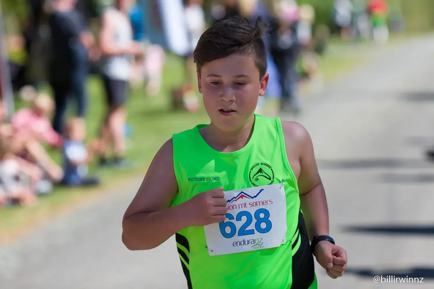 A young boy in a green tank top is running in a race.