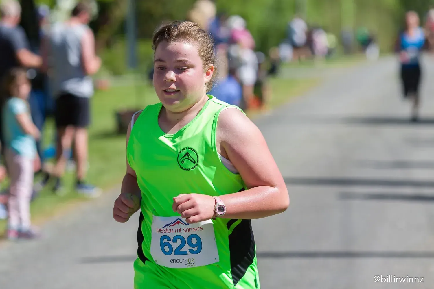 A young girl in a green tank top is running in a race.
