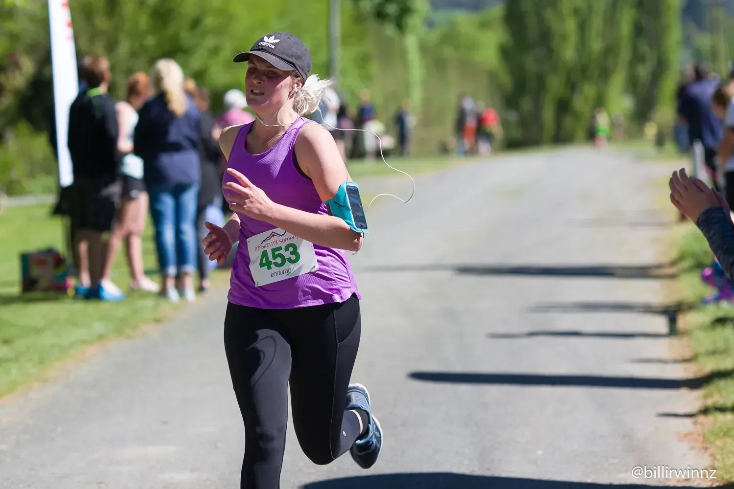 A woman in a purple tank top is running down a road.