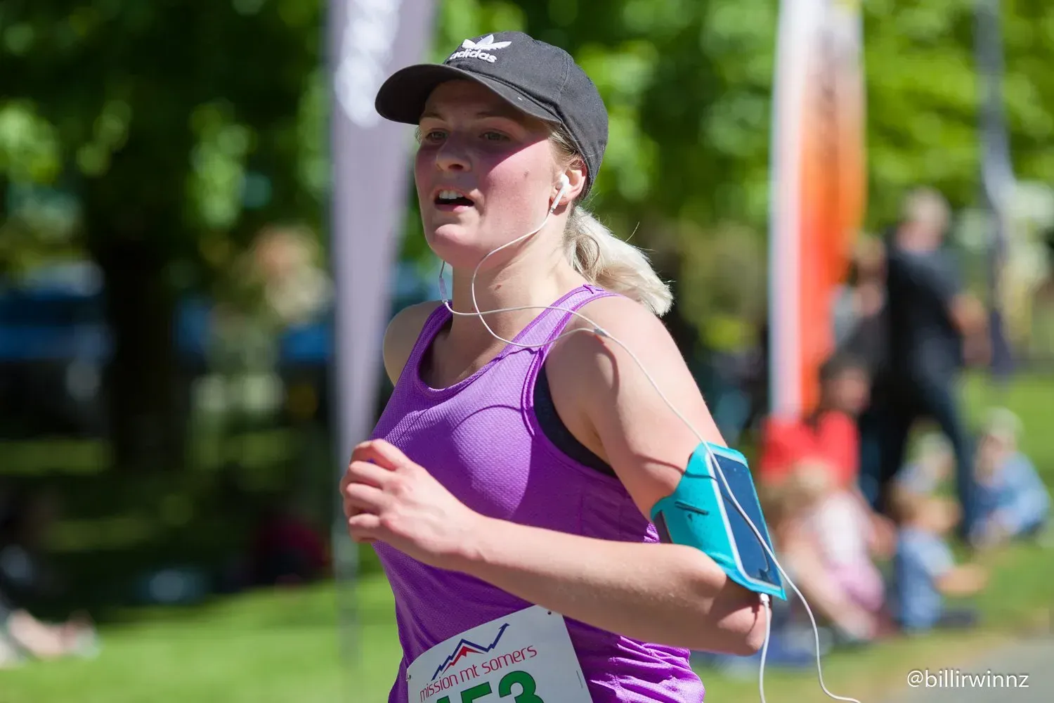 A woman in a purple tank top and black hat is running a marathon.