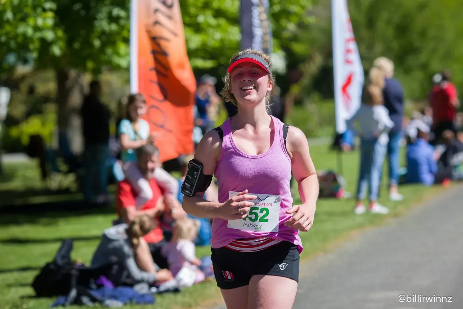 A woman is running a marathon in a park with a number 52 on her shirt.