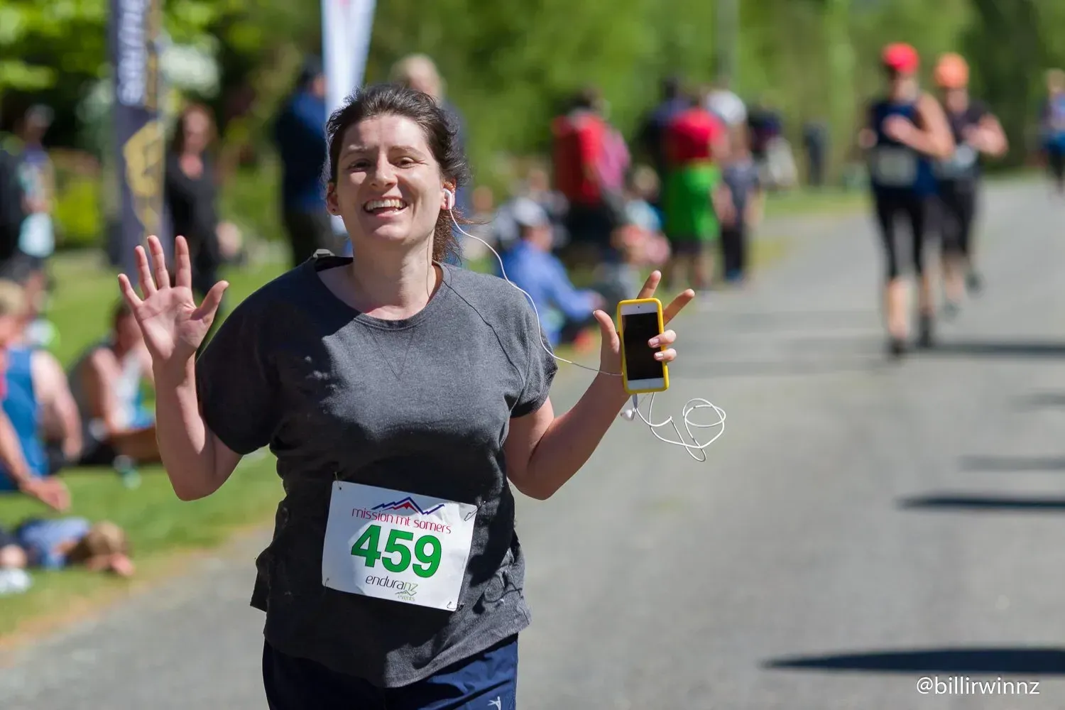 A woman is running in a race and holding a cell phone.