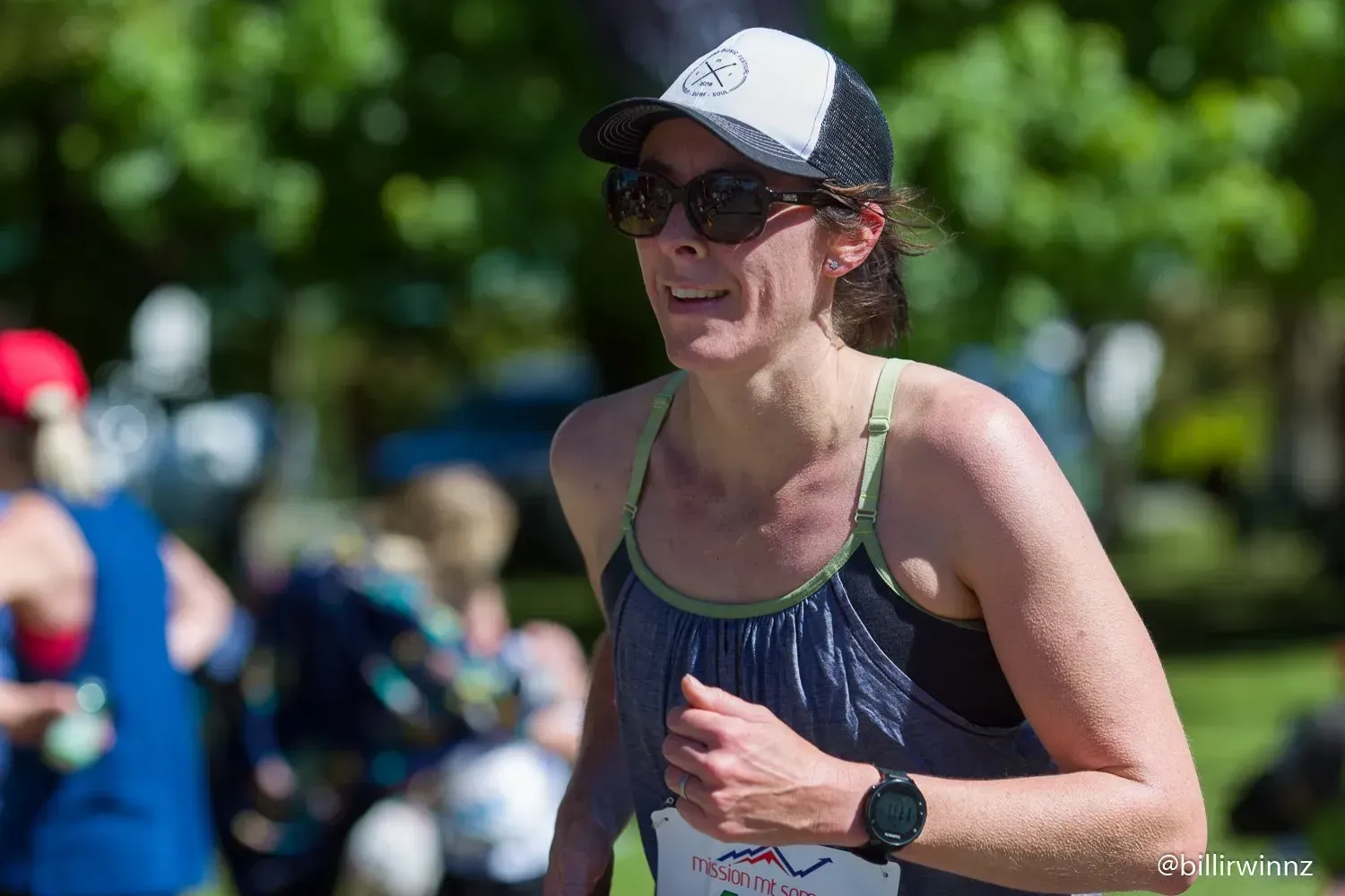 A woman wearing sunglasses and a hat is running in a park.