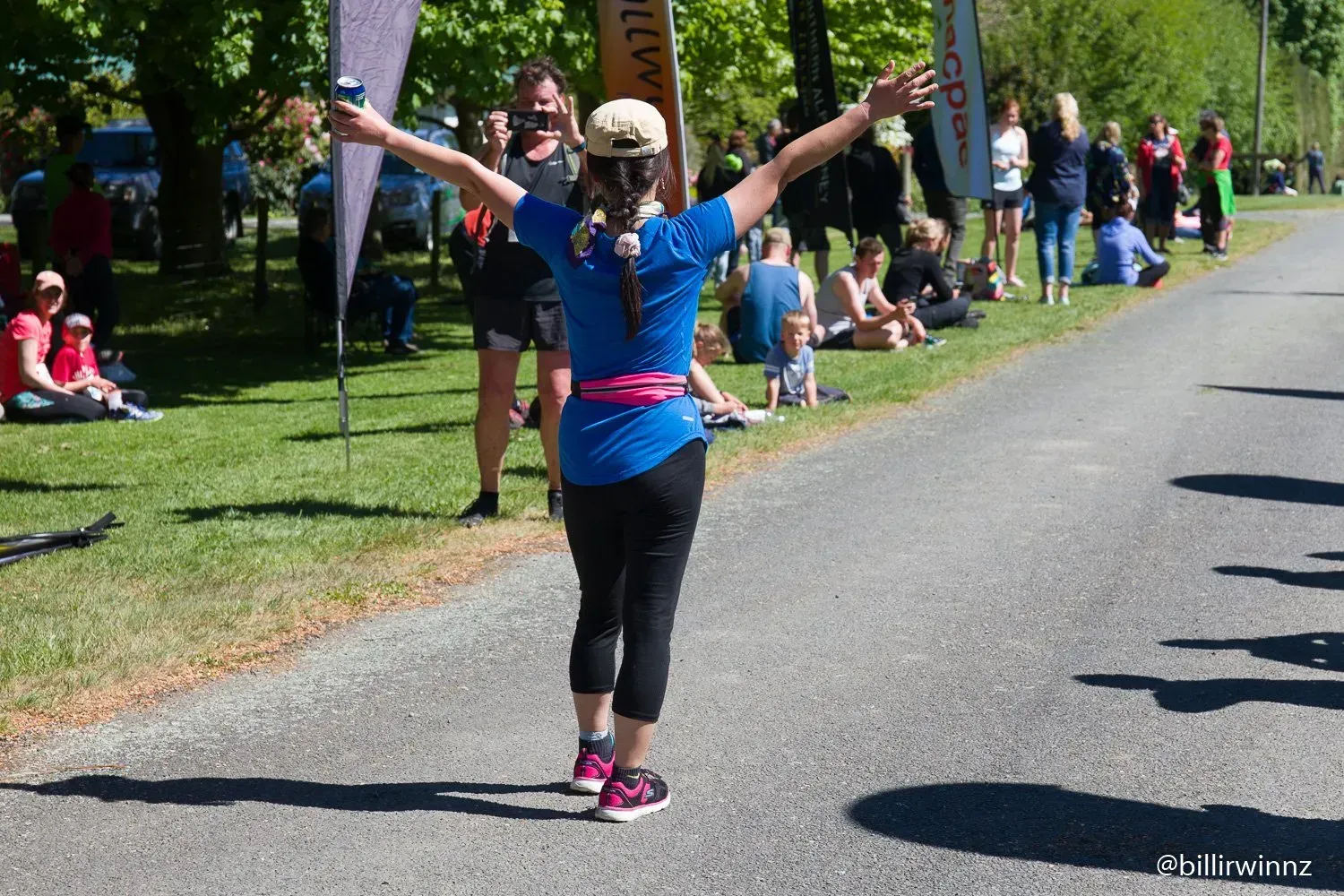 A woman in a blue shirt is standing on a road with her arms outstretched.