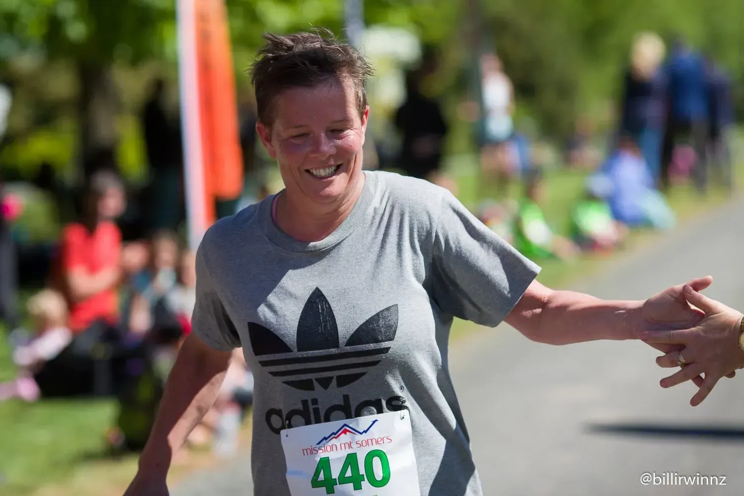 A woman wearing an adidas shirt is shaking hands with another person.