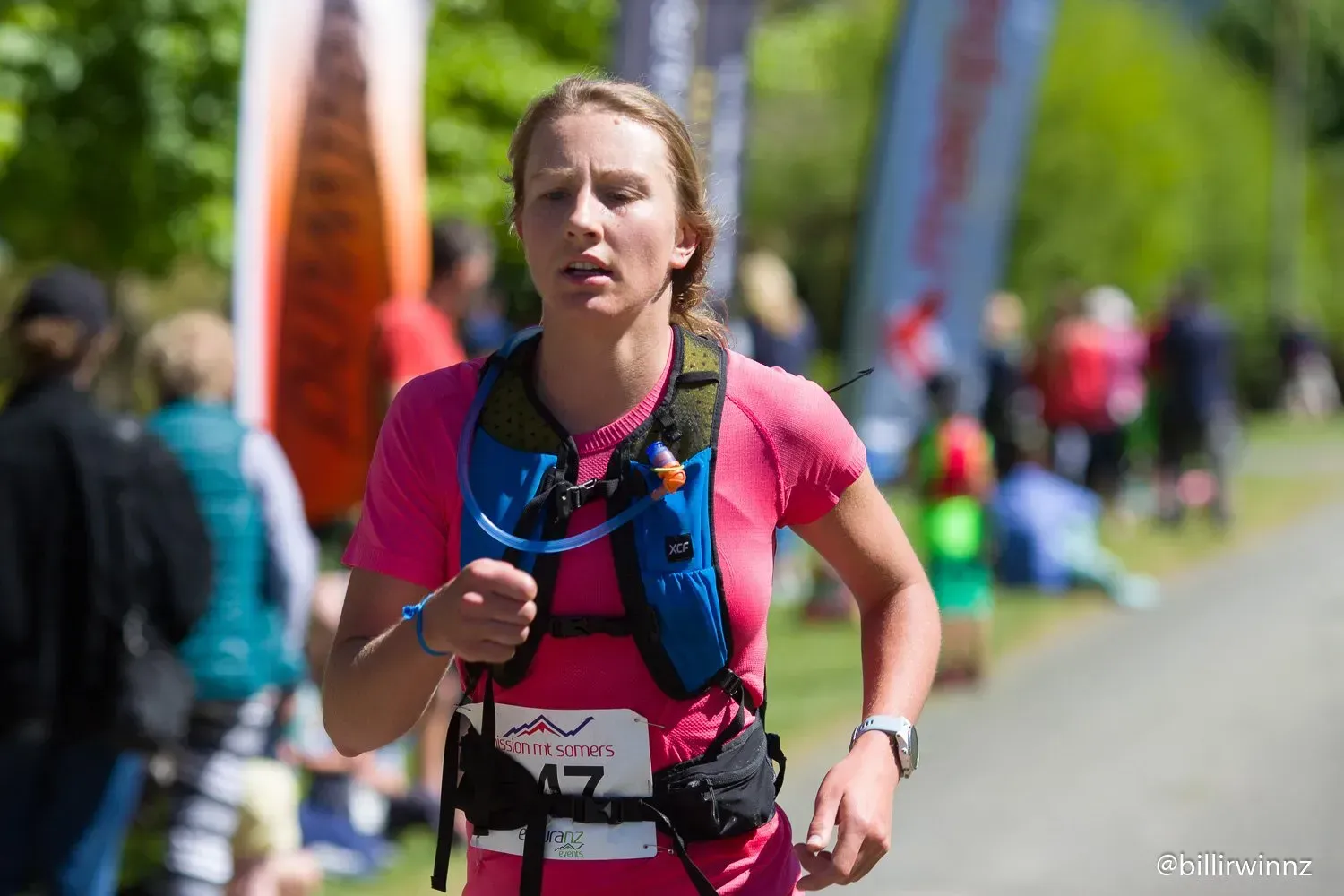 A woman is running in a race with a water pack on her back.