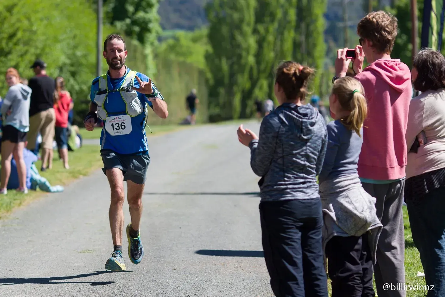 A man is running down a road with a number on his shirt.