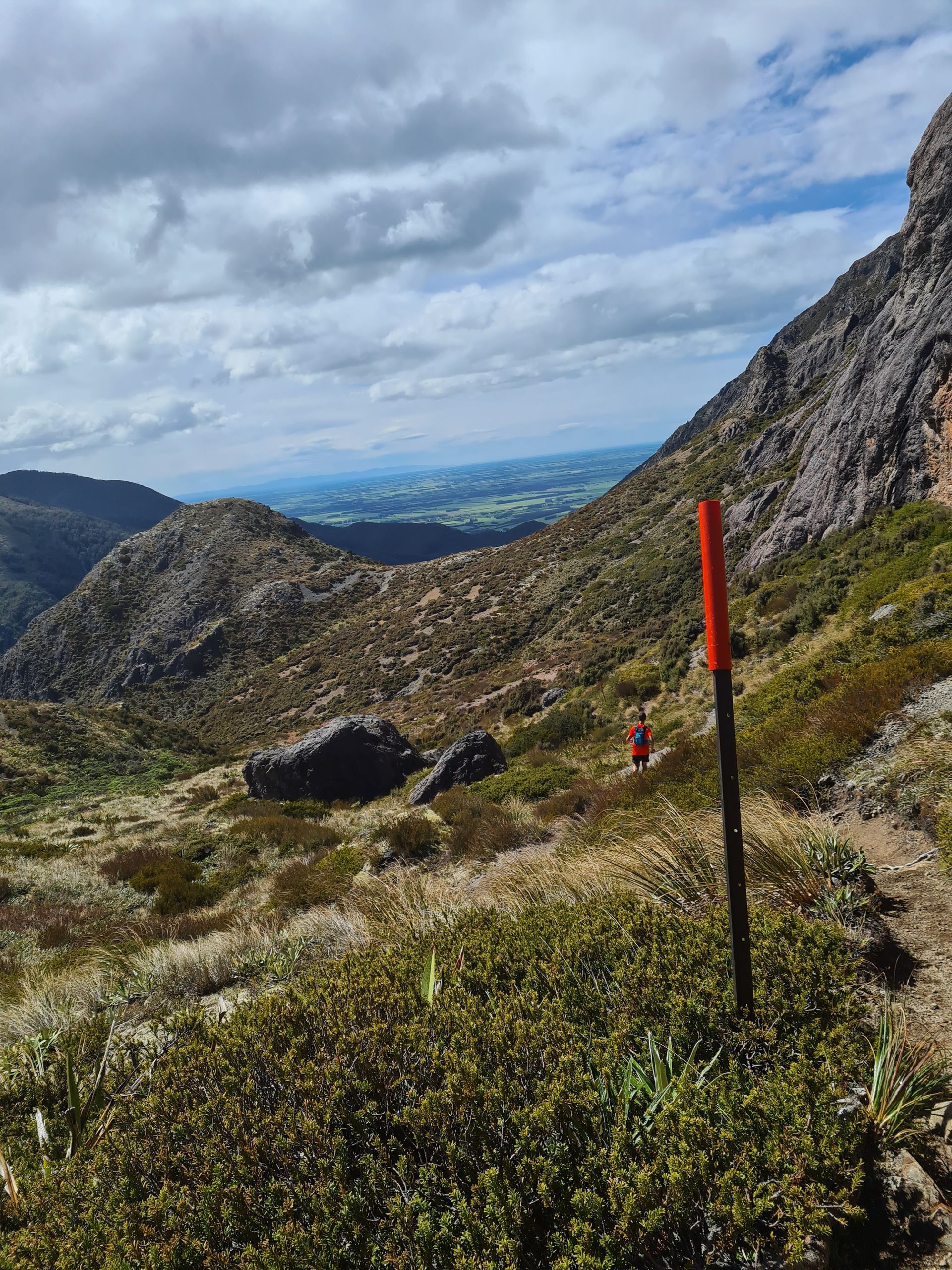 A person is standing on a trail in the mountains with a red pole in the foreground.