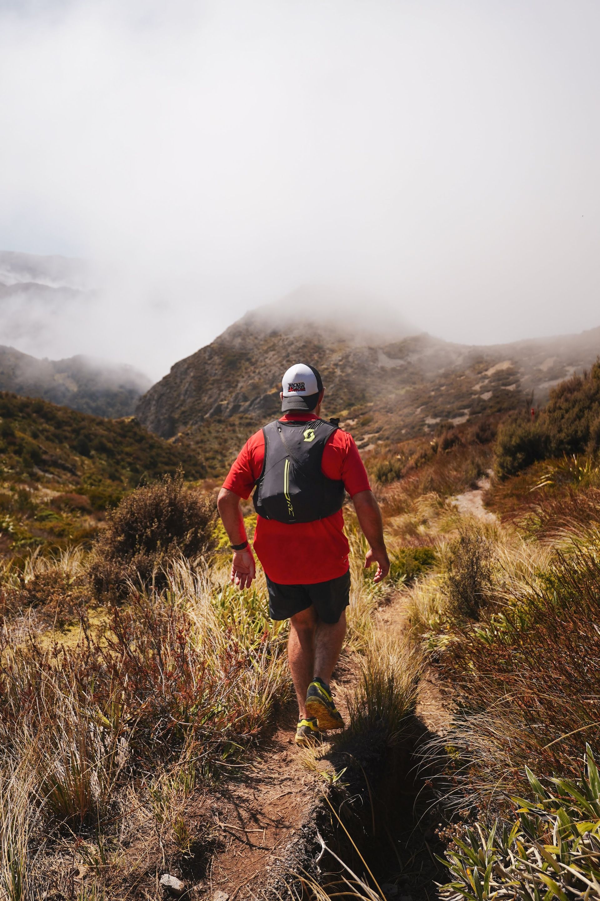 A man is walking down a trail in the mountains.