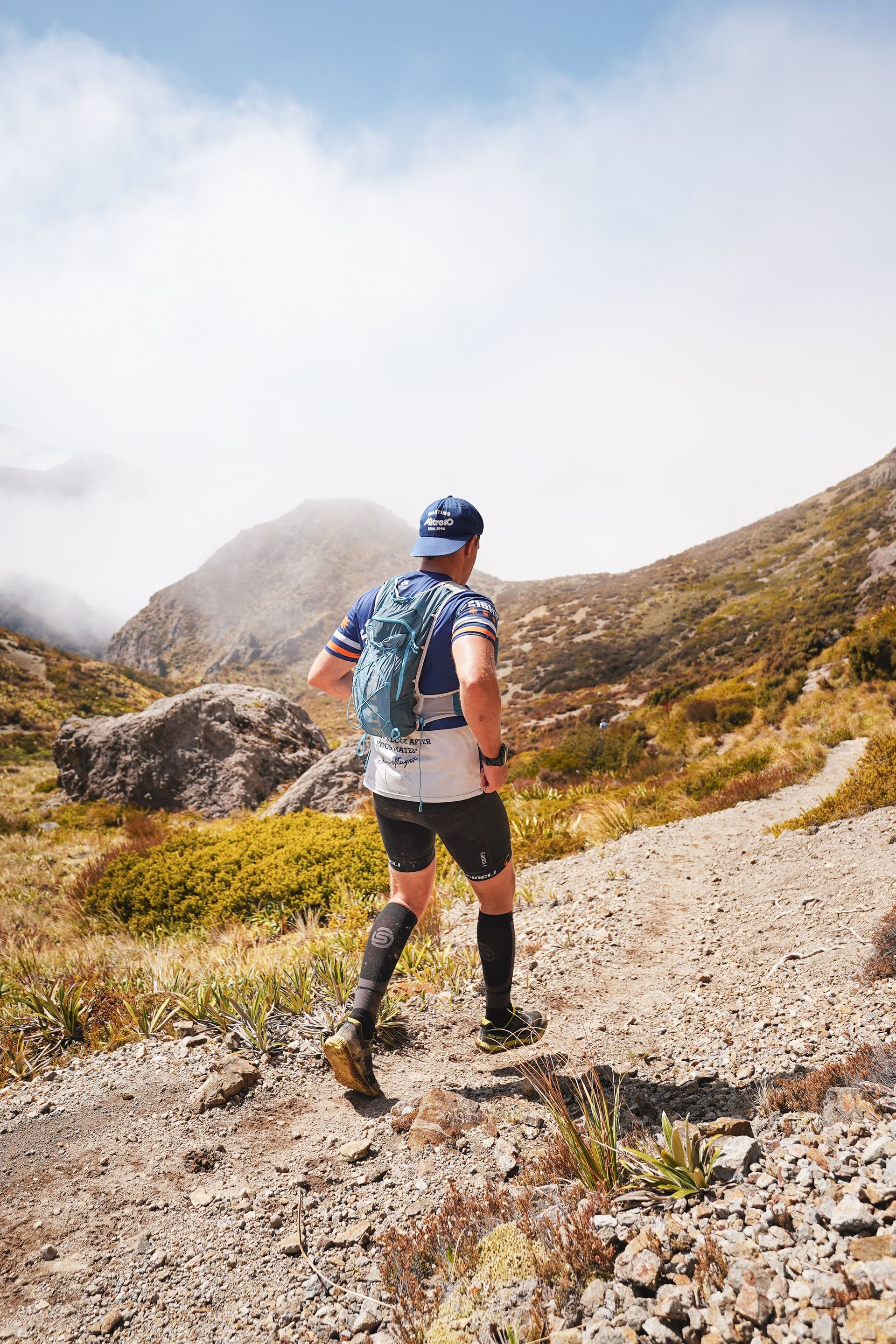 A man with a backpack is running on a trail in the mountains.