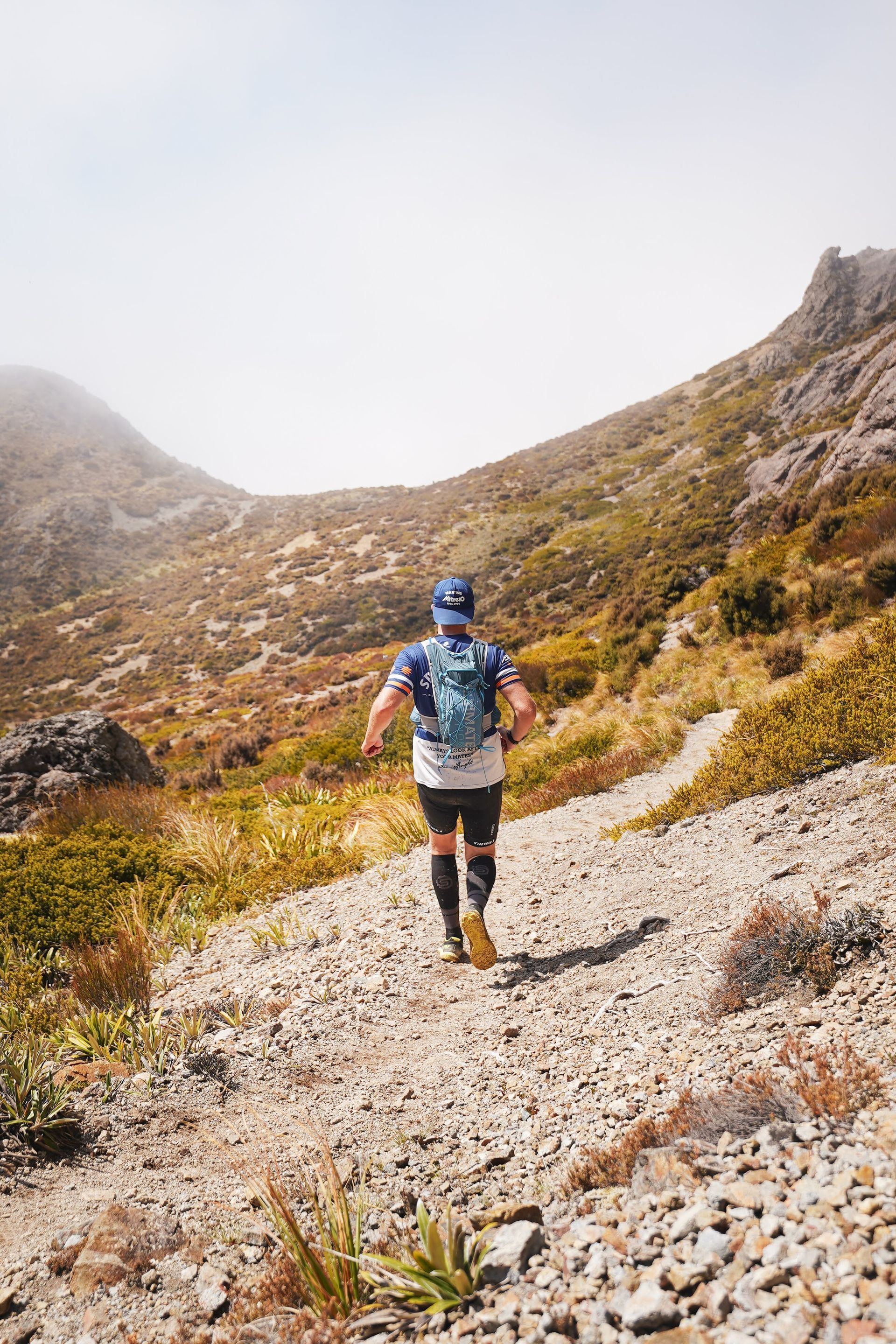 A man is running down a rocky trail in the mountains.