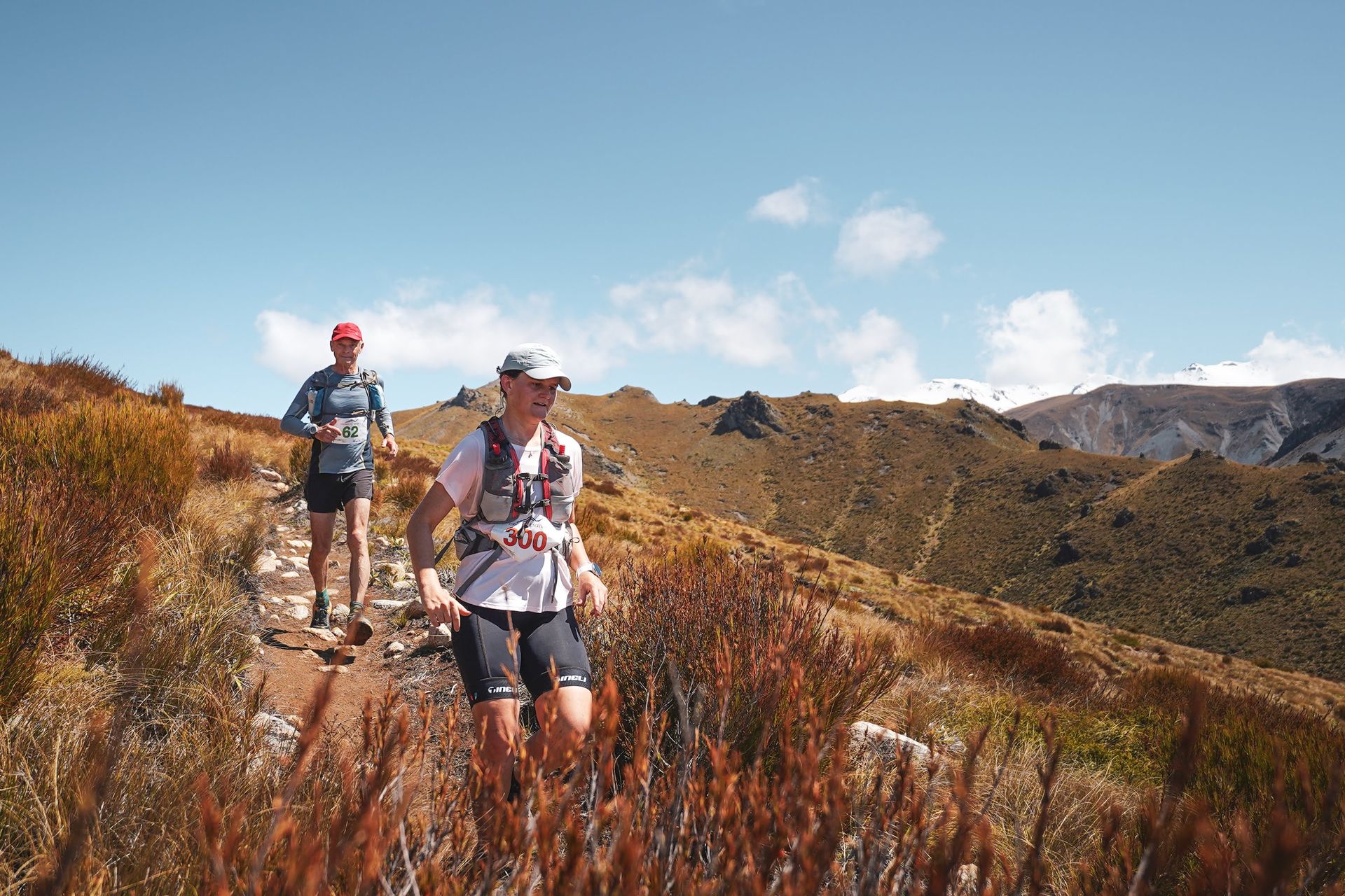 Two people are running on a trail in the mountains.