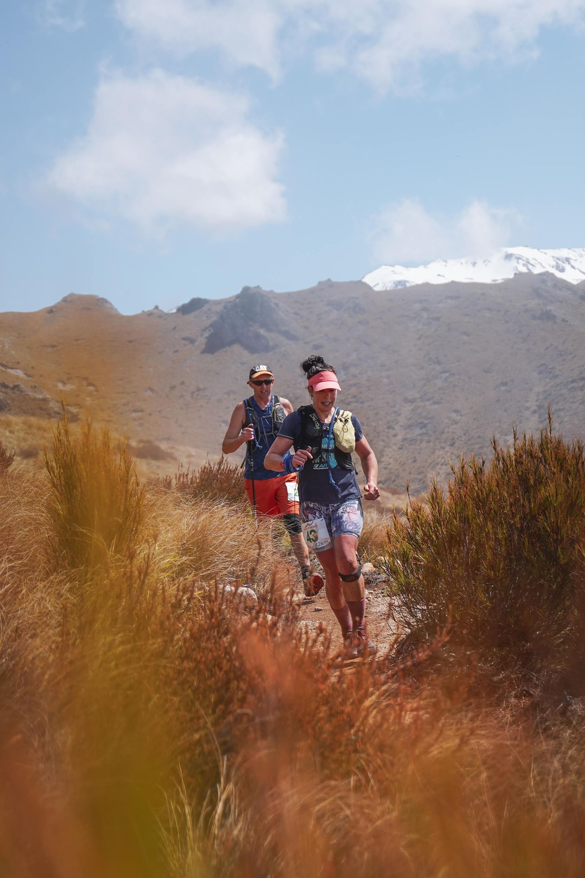 Two people are running on a trail in the mountains.