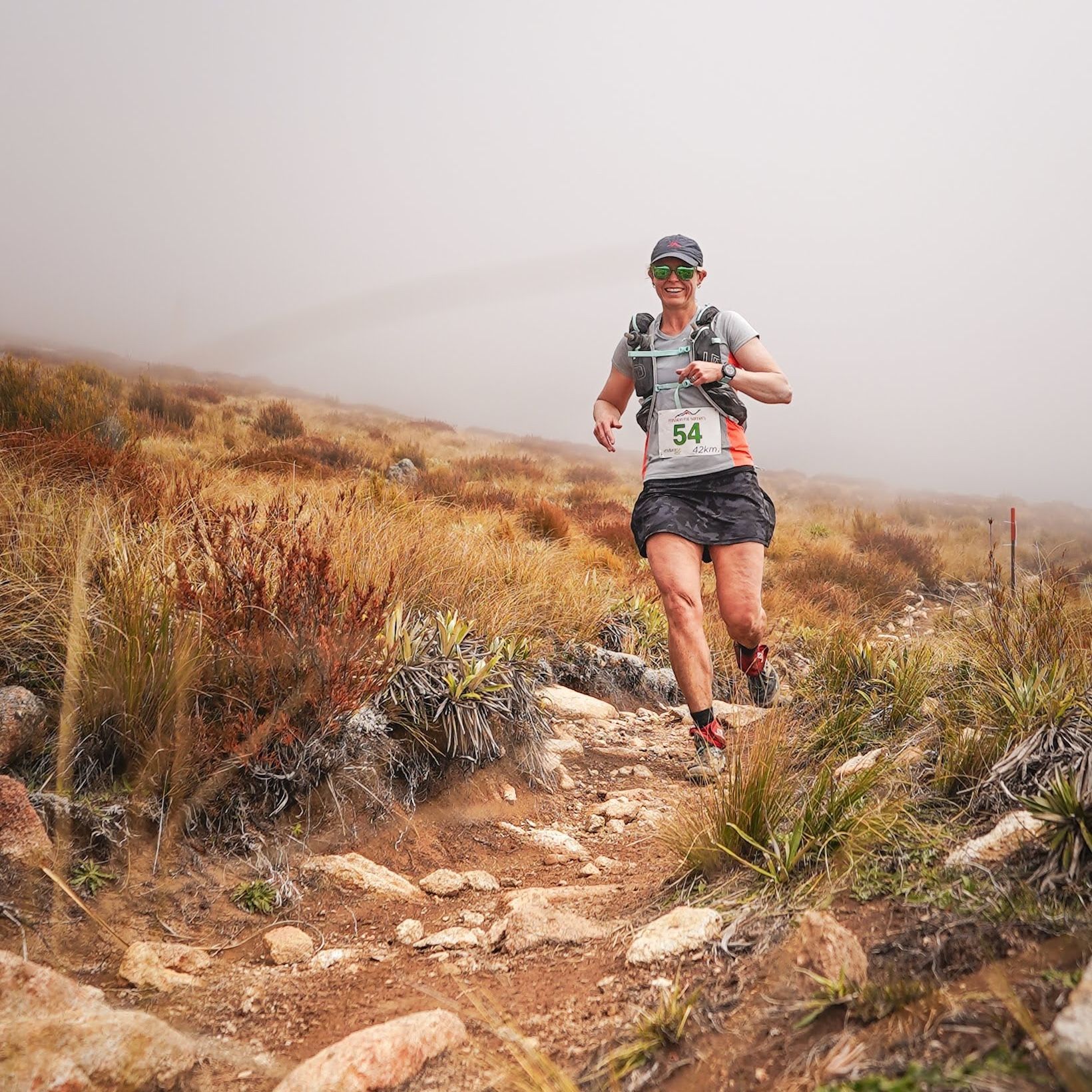 A woman is running on a trail in the mountains.