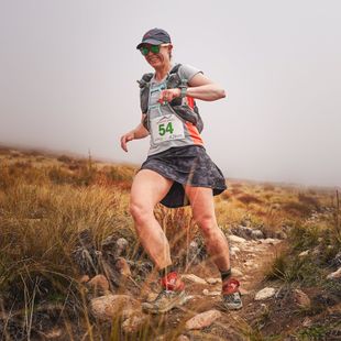 A woman is running on a trail with a number 54 on her shirt.