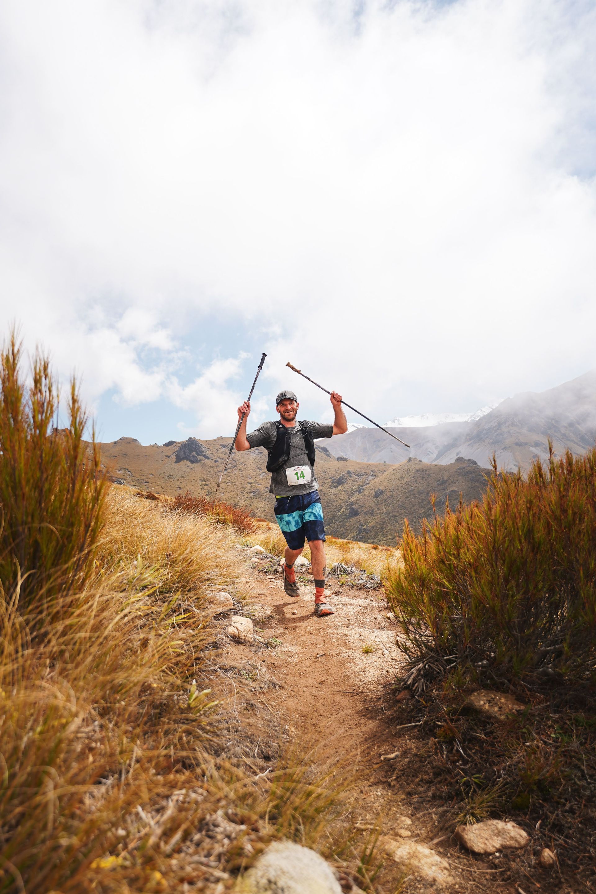 A man is running on a trail in the mountains holding a pole.