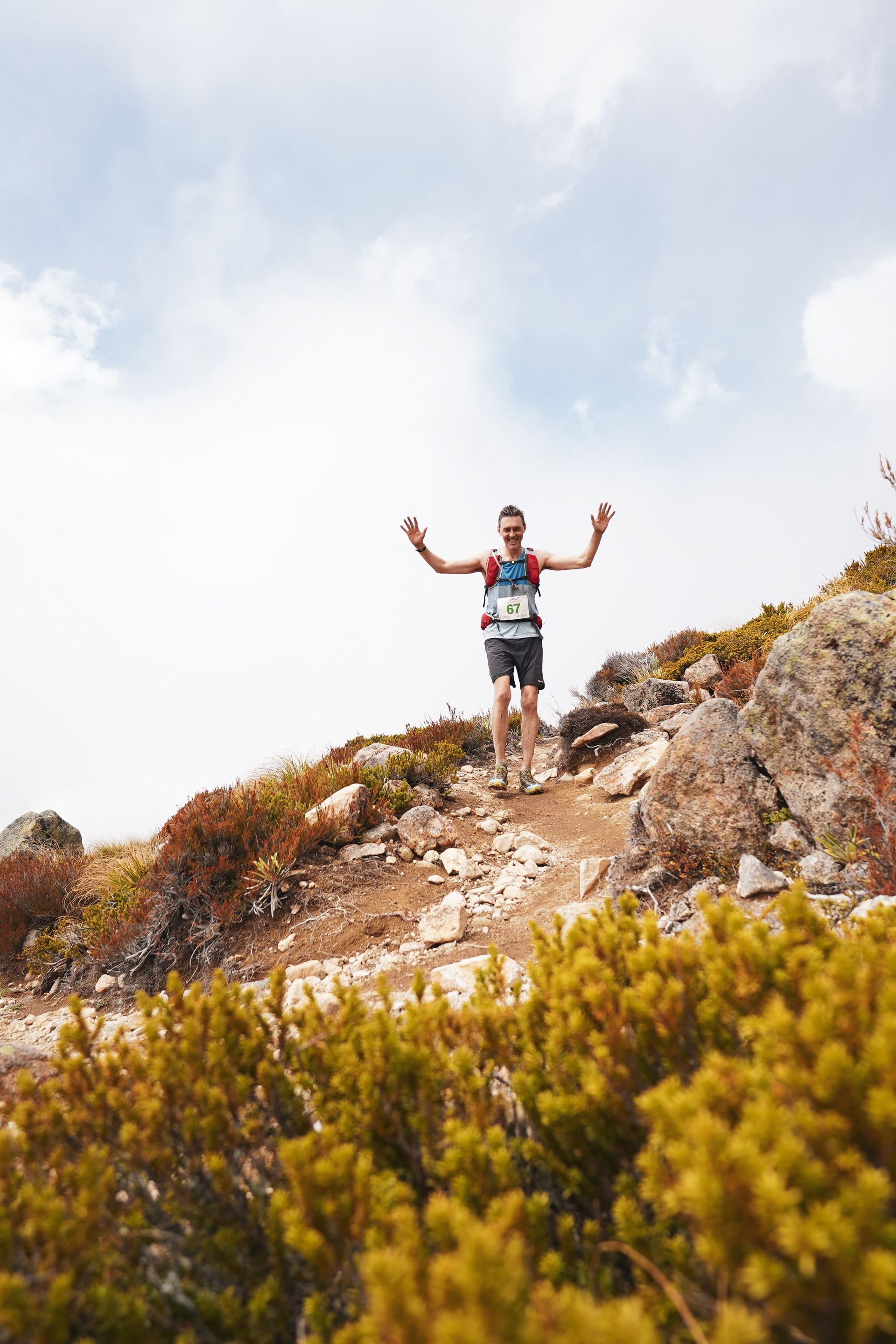 A man is standing on top of a rocky hill with his arms outstretched.