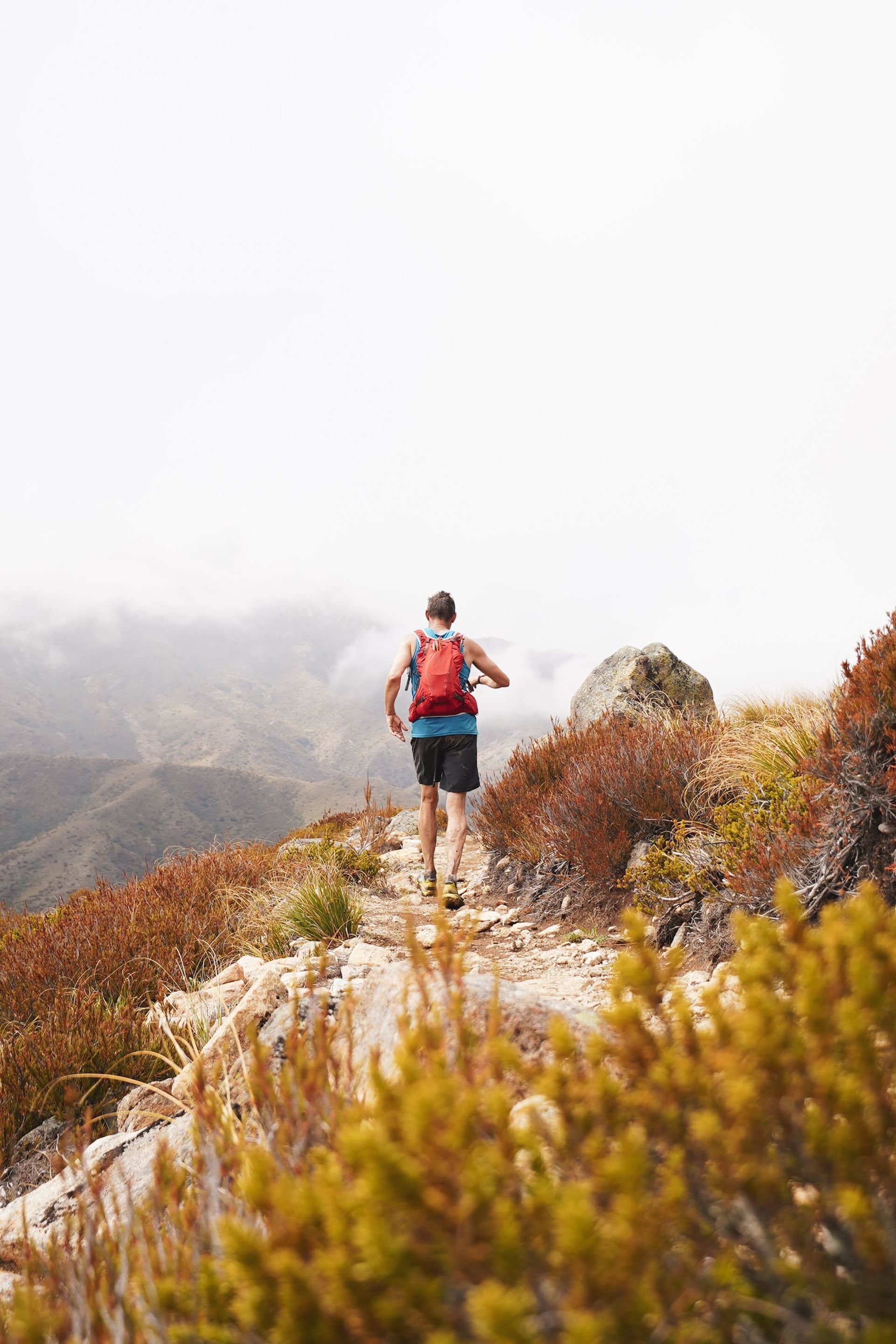 A man with a backpack is running on a trail in the mountains.
