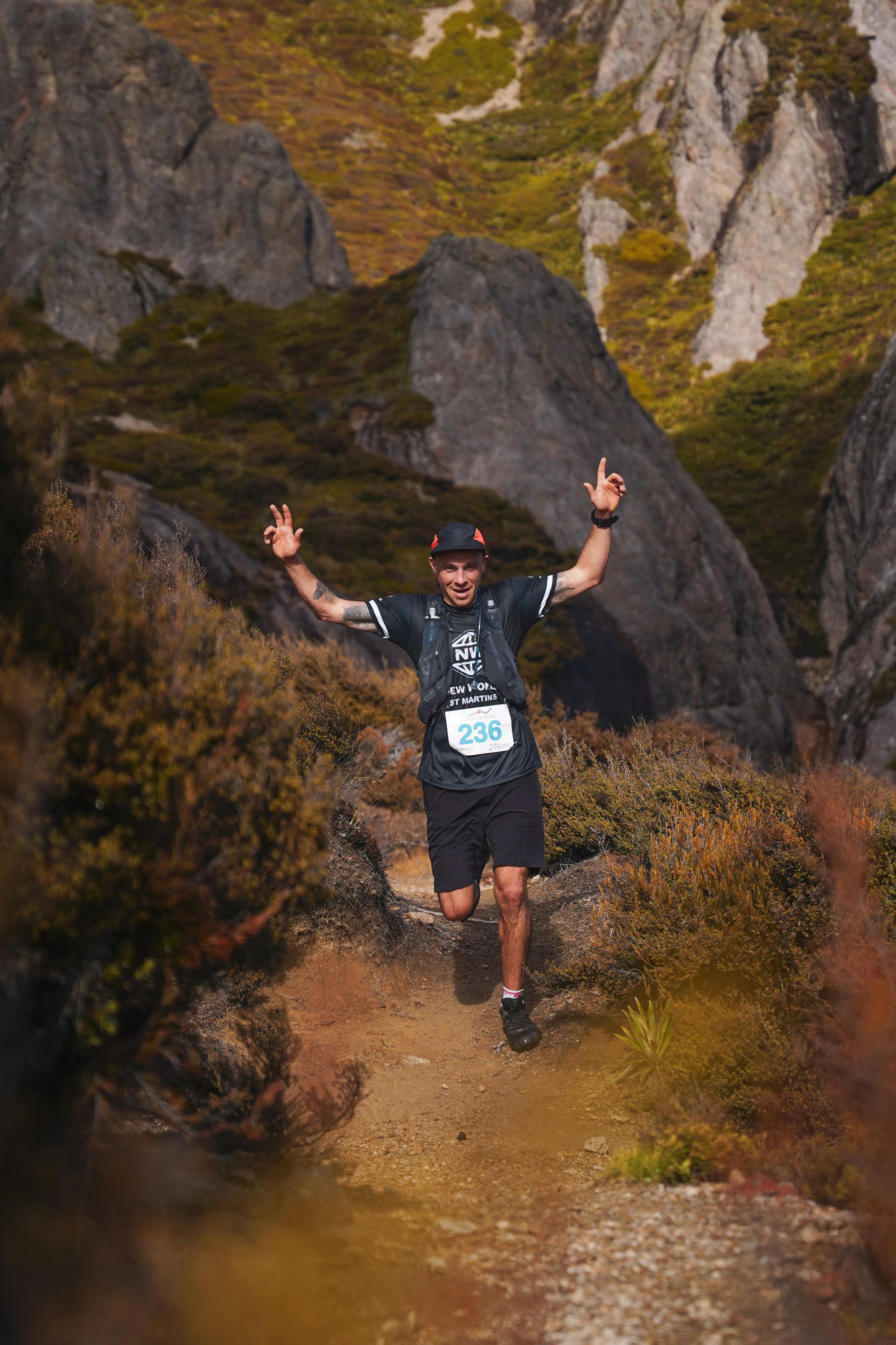 A man is running on a trail in the mountains with his arms in the air.