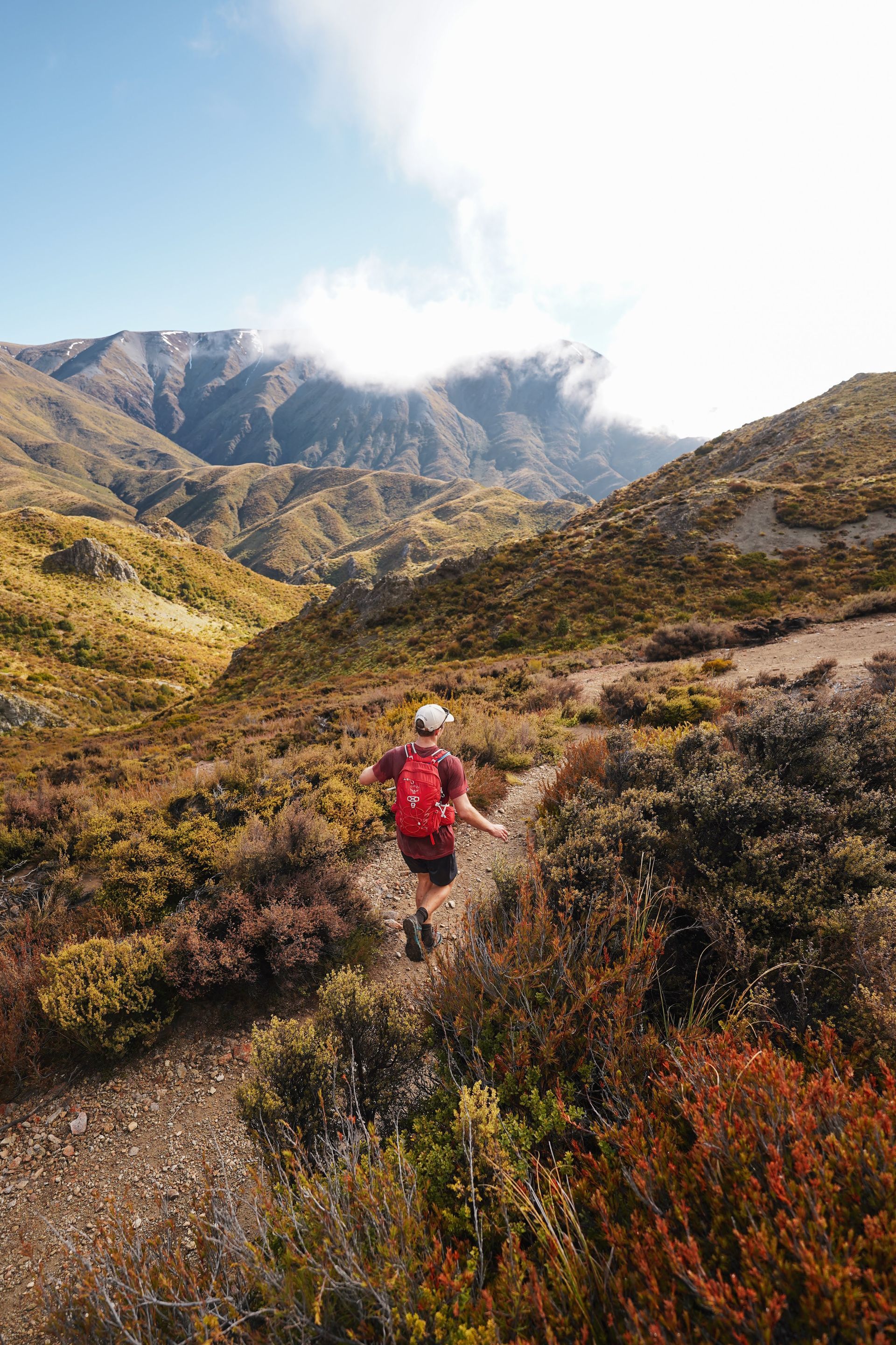 A man with a backpack is walking down a trail in the mountains.