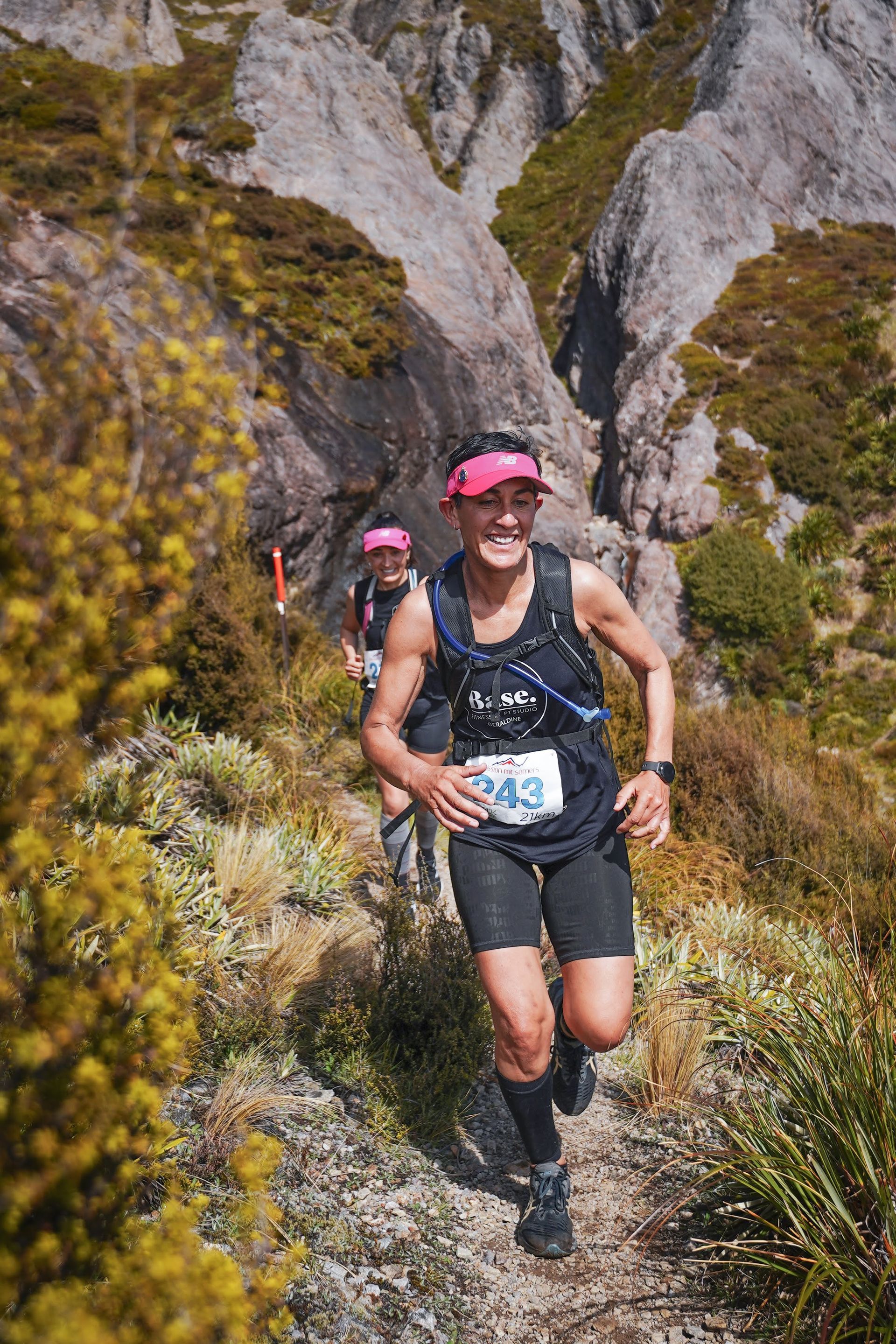 A woman is running down a trail in the mountains.