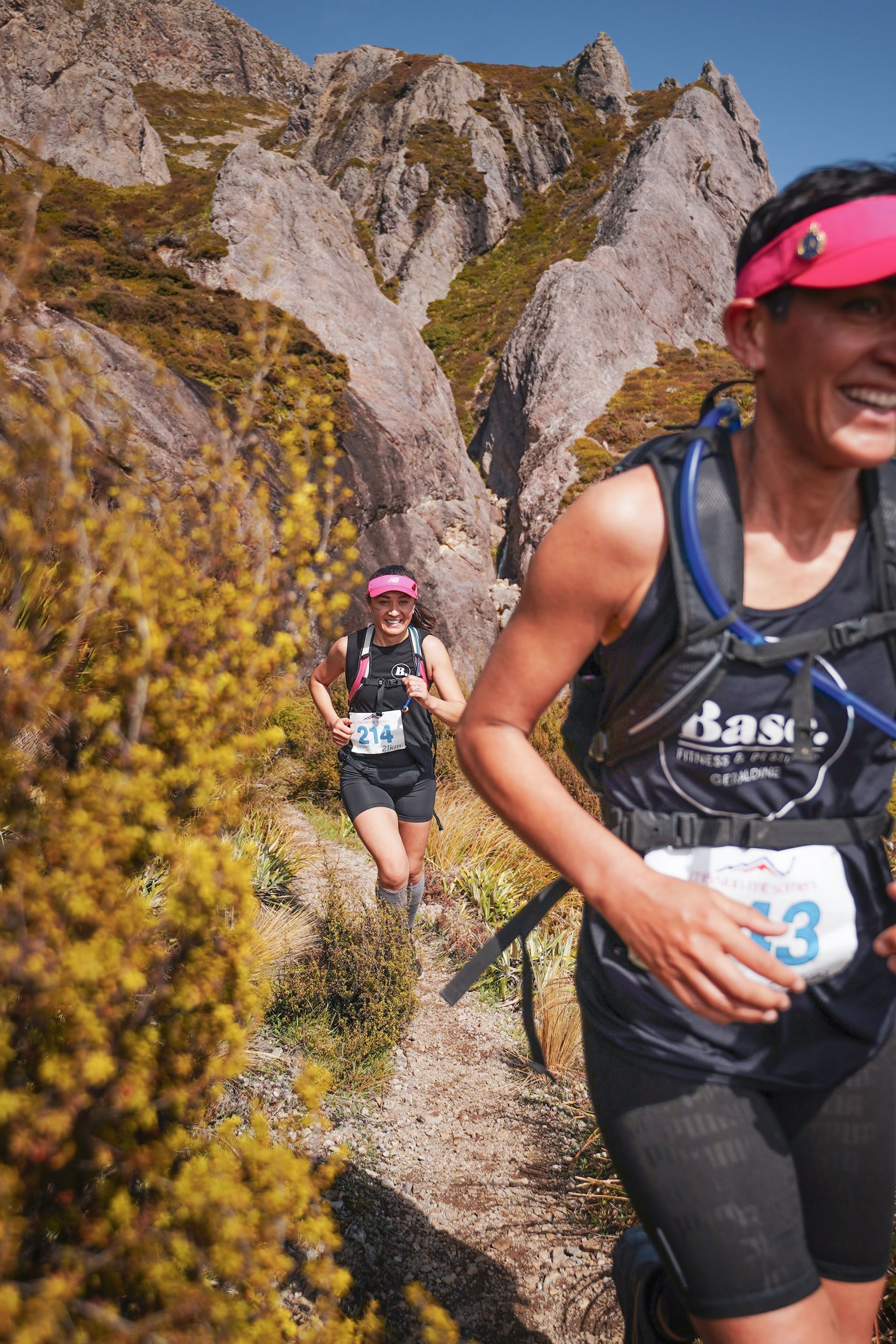 Two women are running on a trail in the mountains.