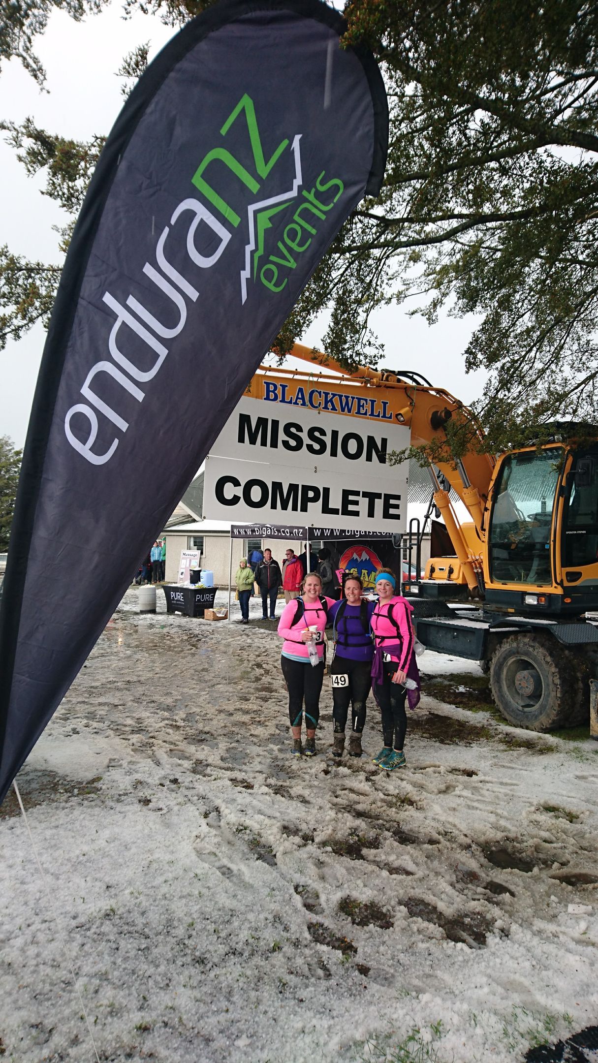A group of people are standing in the mud in front of a sign that says `` mission complete ''.