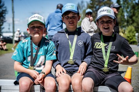 Three young boys wearing medals are sitting on a bench.