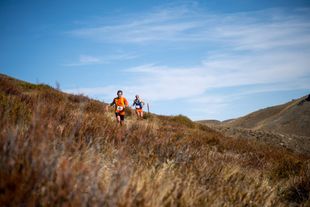 Two people are running up a hill in a field.