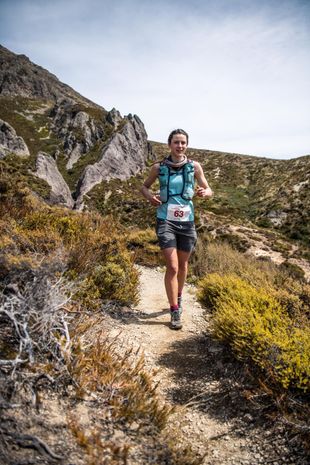 A woman is running on a trail in the mountains.