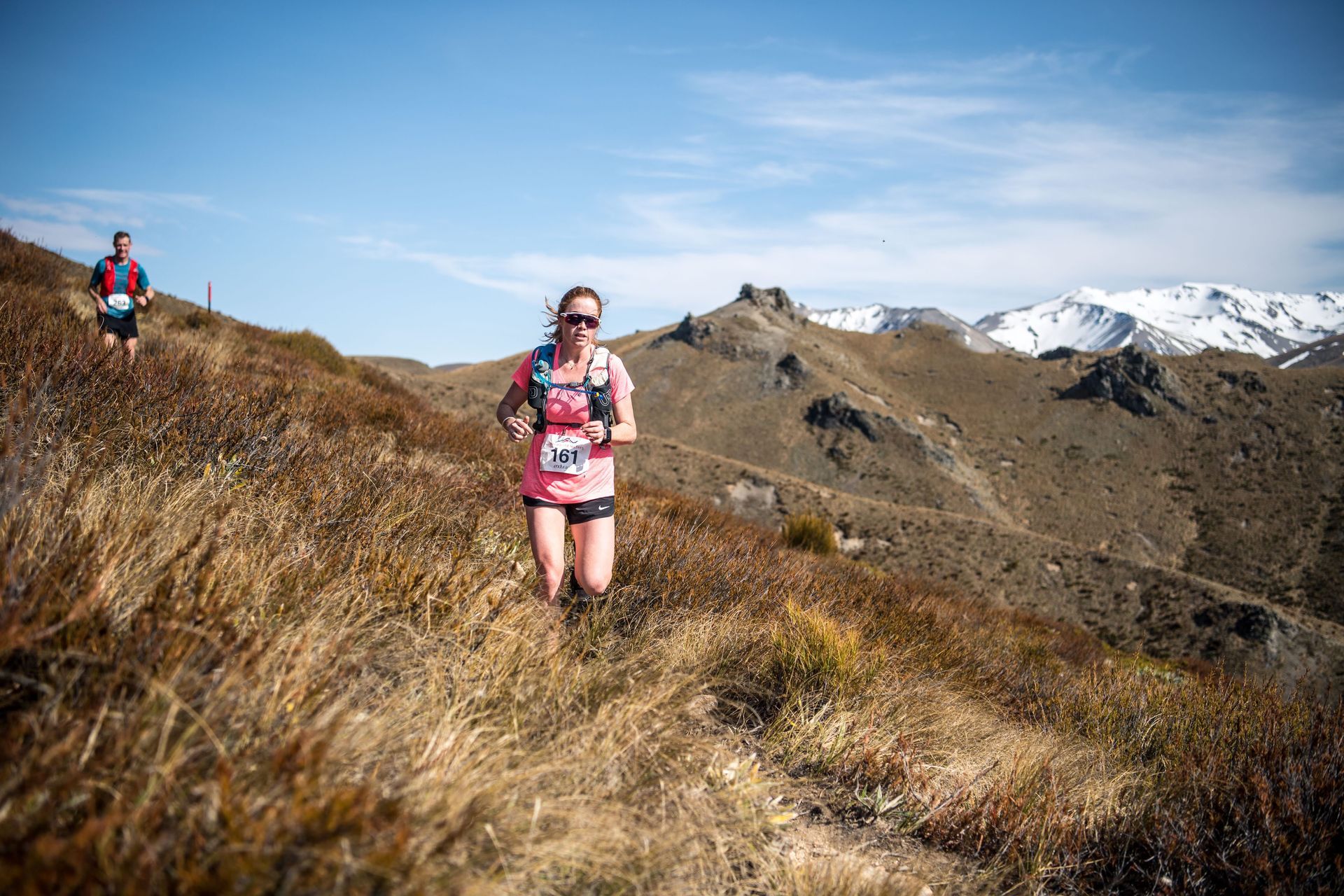 A man and a woman are running on a trail in the mountains.