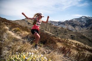 A woman is running on a trail in the mountains.