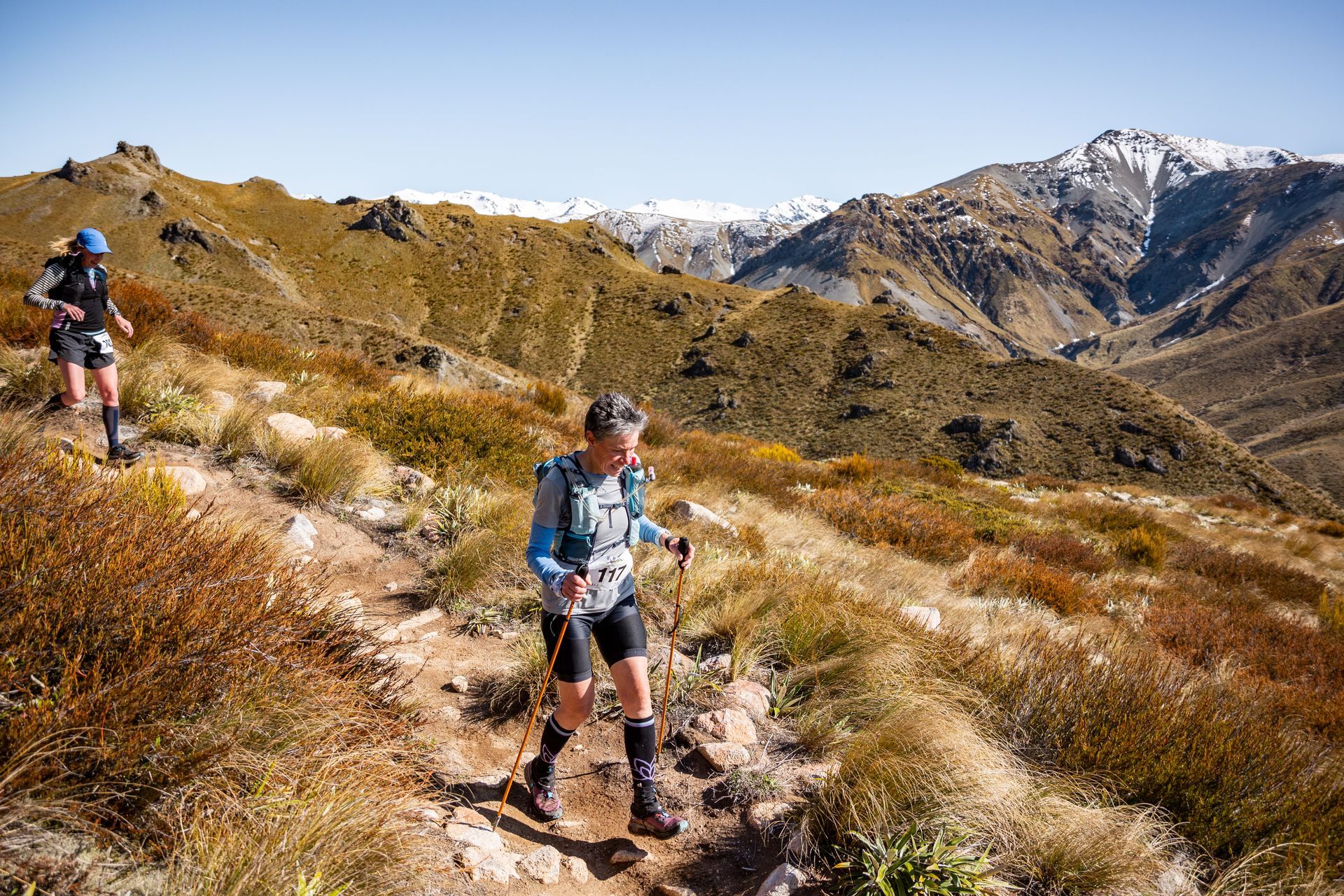 Two people are running on a trail in the mountains.