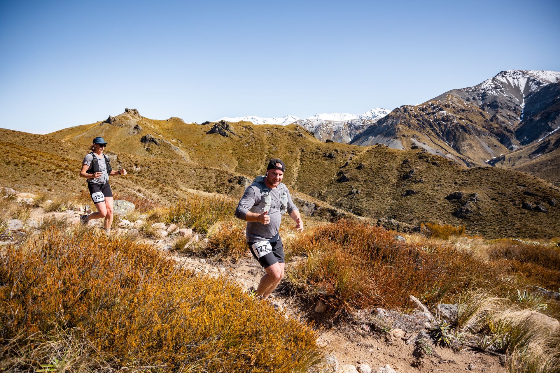 A man and a woman are running on a trail in the mountains.