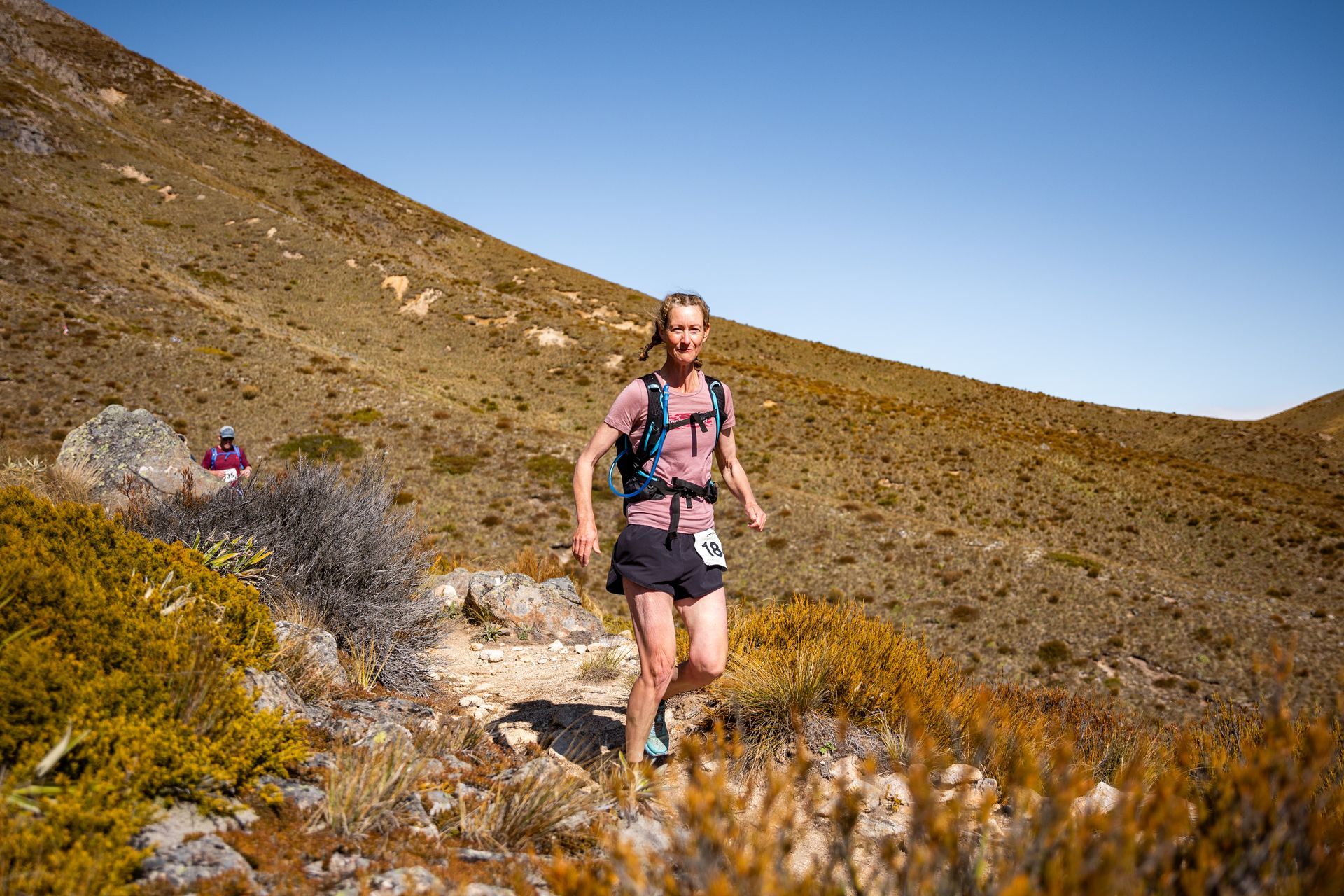 A woman is running on a trail in the mountains.