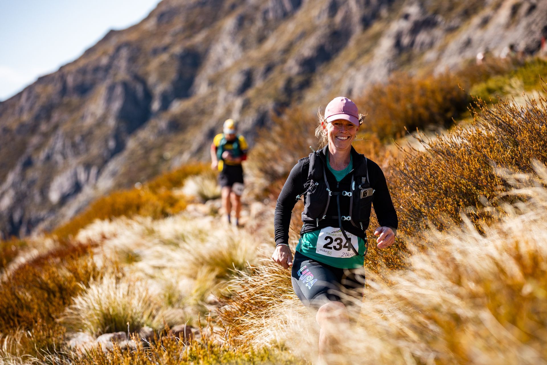Two people are running on a trail in the mountains.
