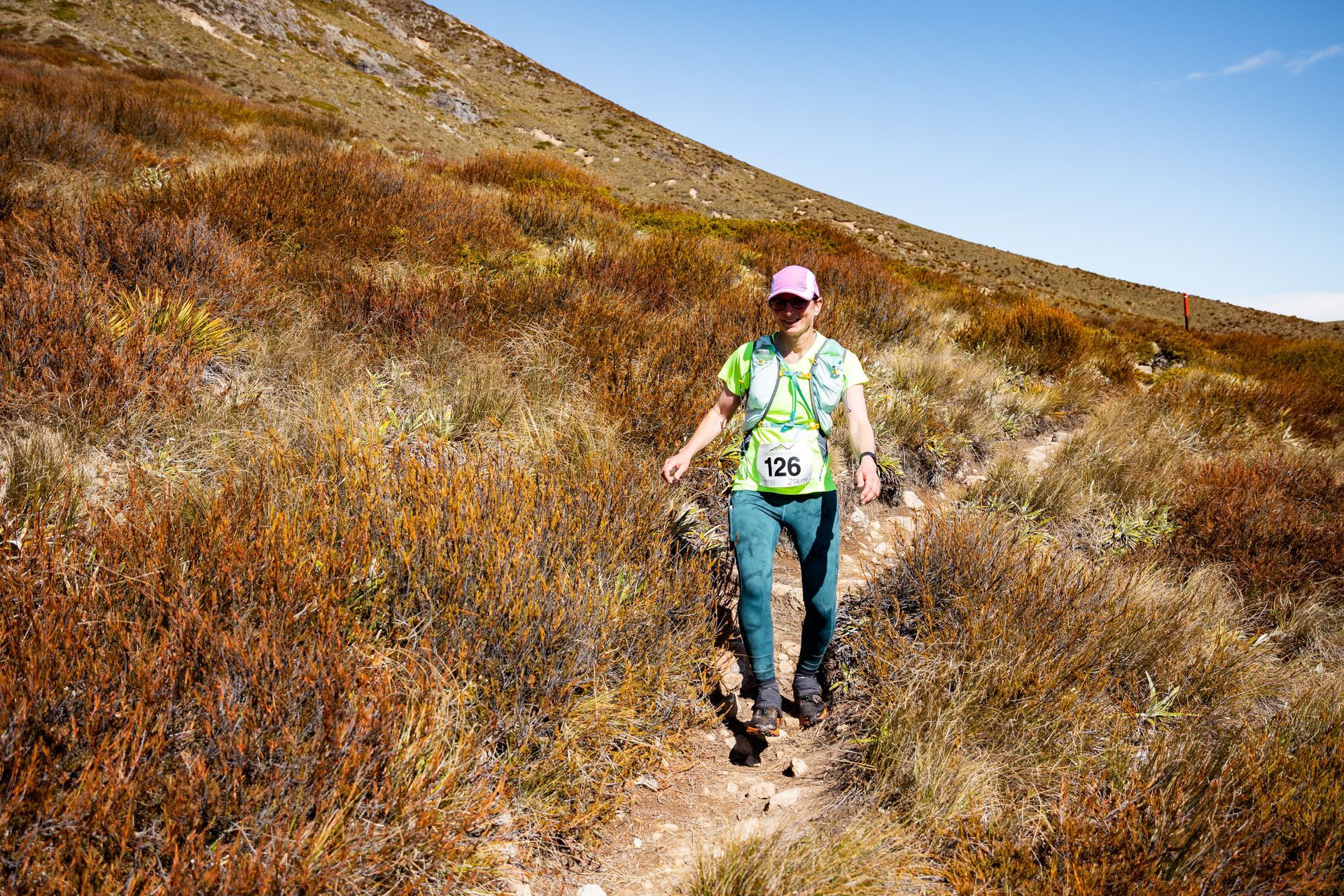 A woman is walking down a trail on a hill.
