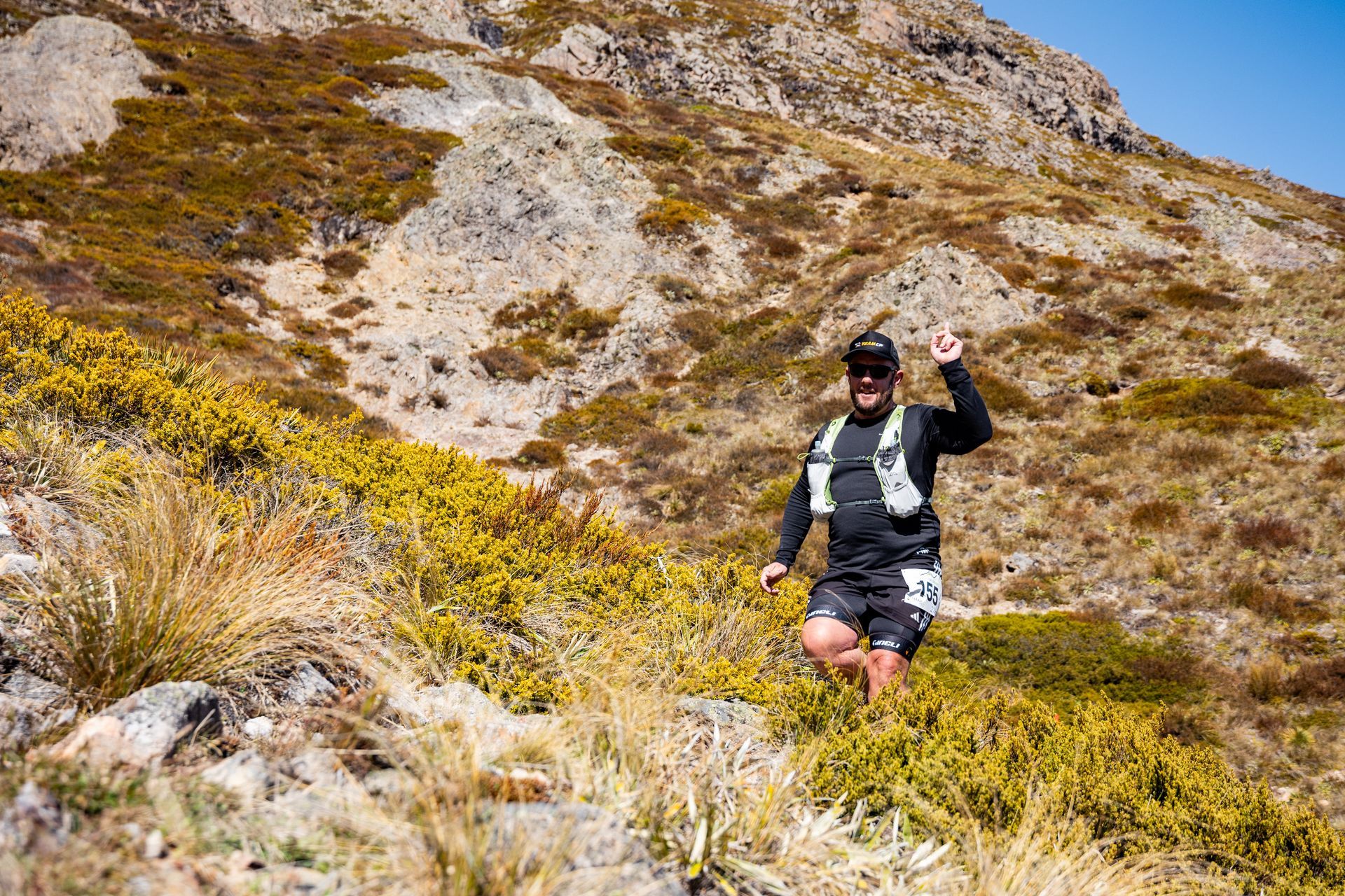 A man is sitting on top of a hill giving a thumbs up.