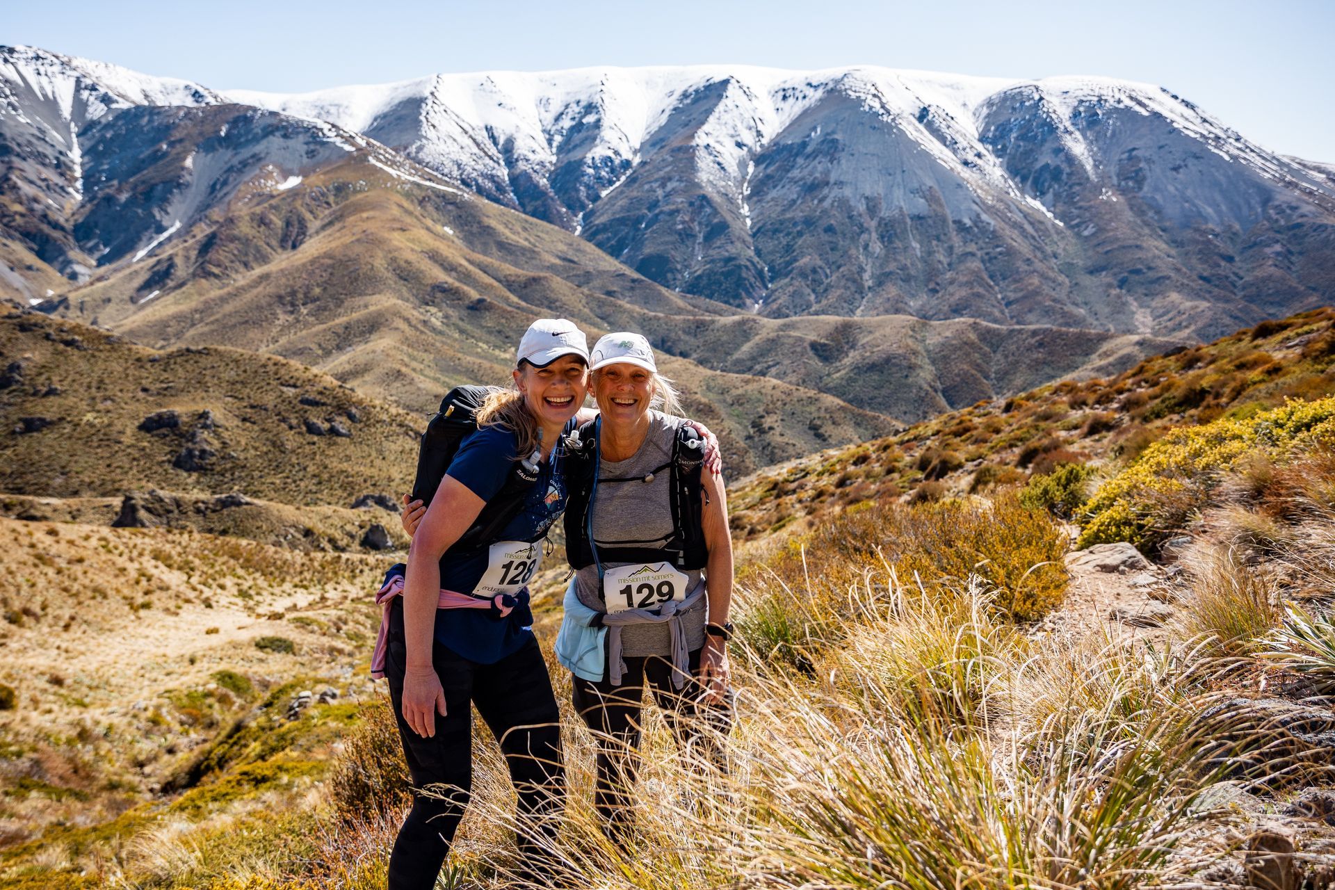Two women are posing for a picture in front of a snowy mountain.