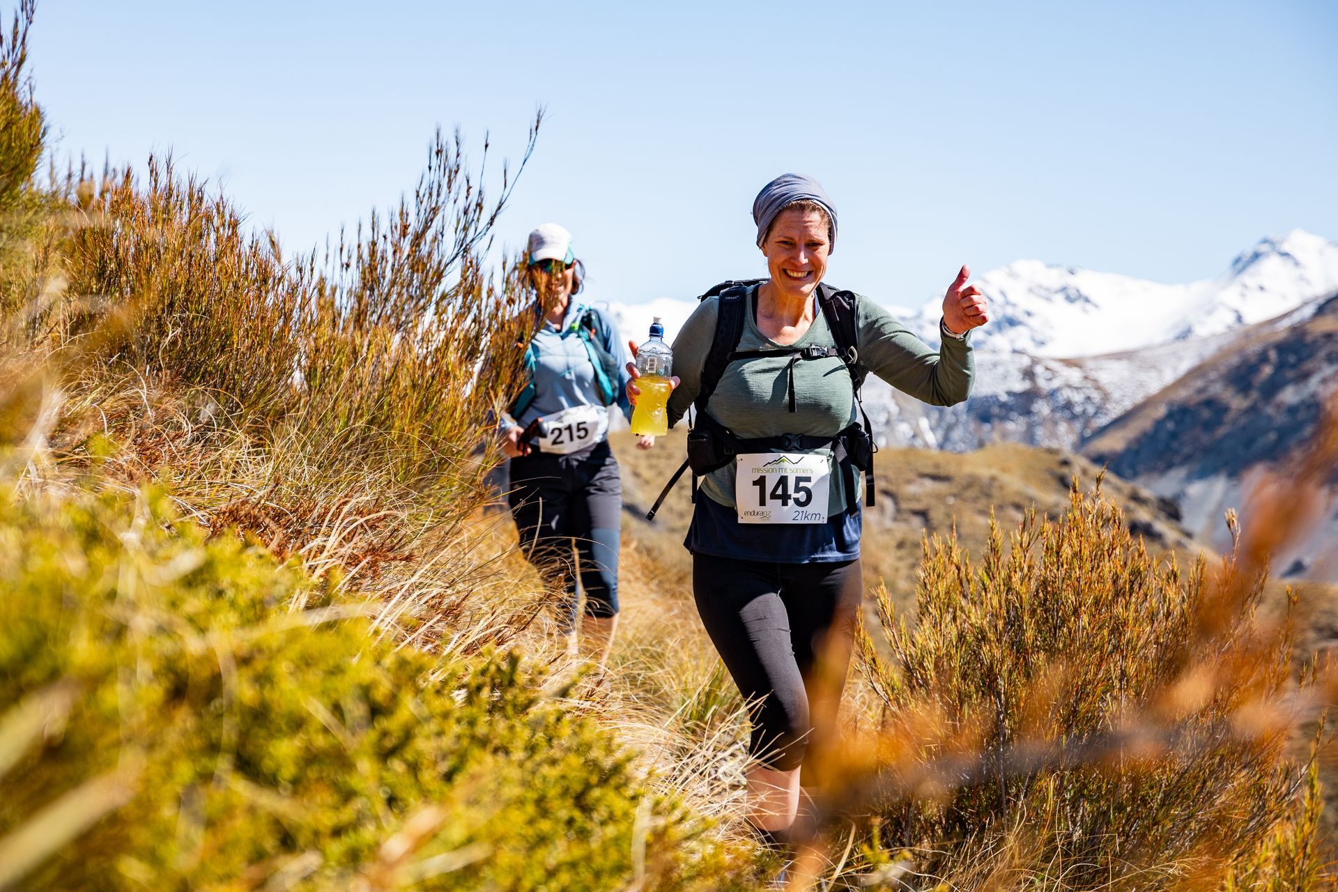 Two women are running on a trail in the mountains.