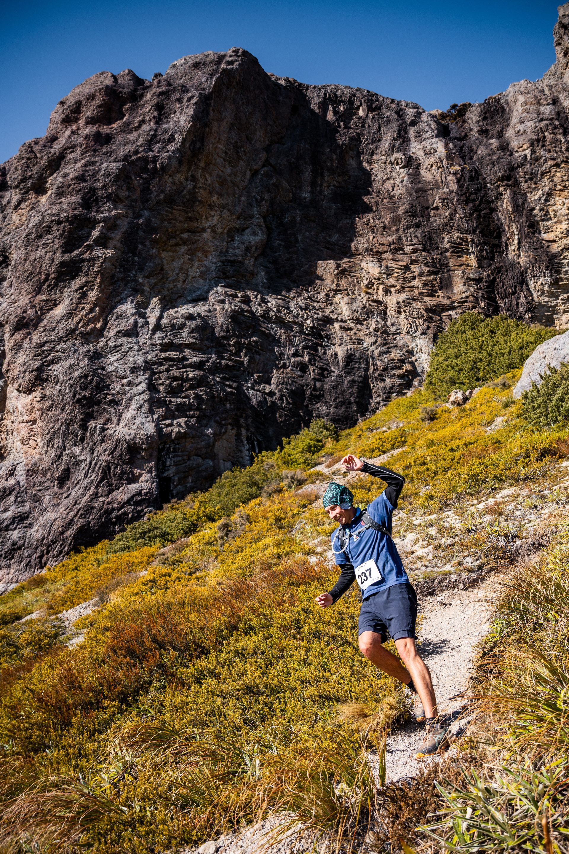A man is running down a trail in the mountains.
