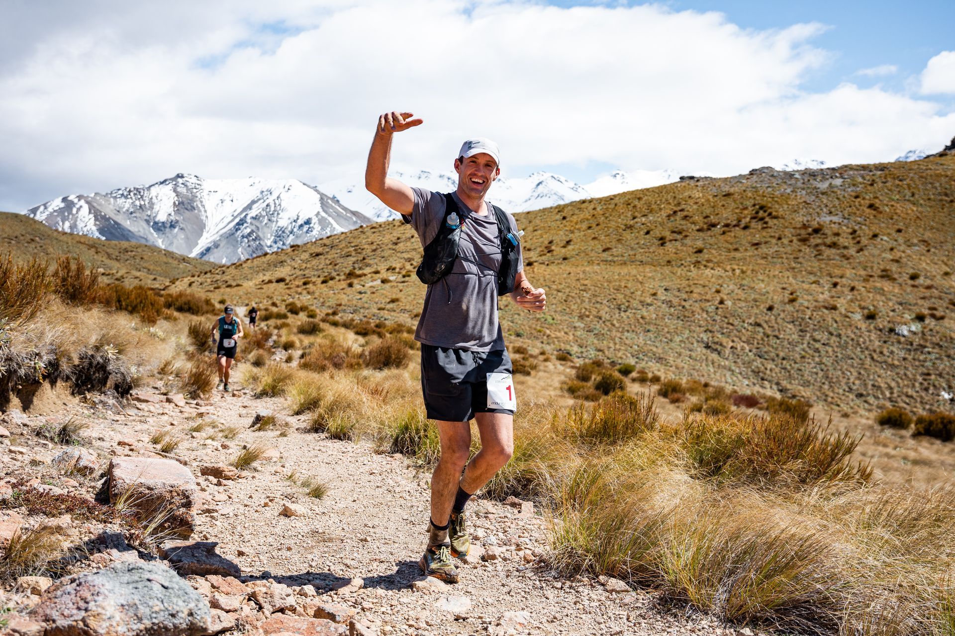 A man is running on a dirt trail in the desert with mountains in the background.